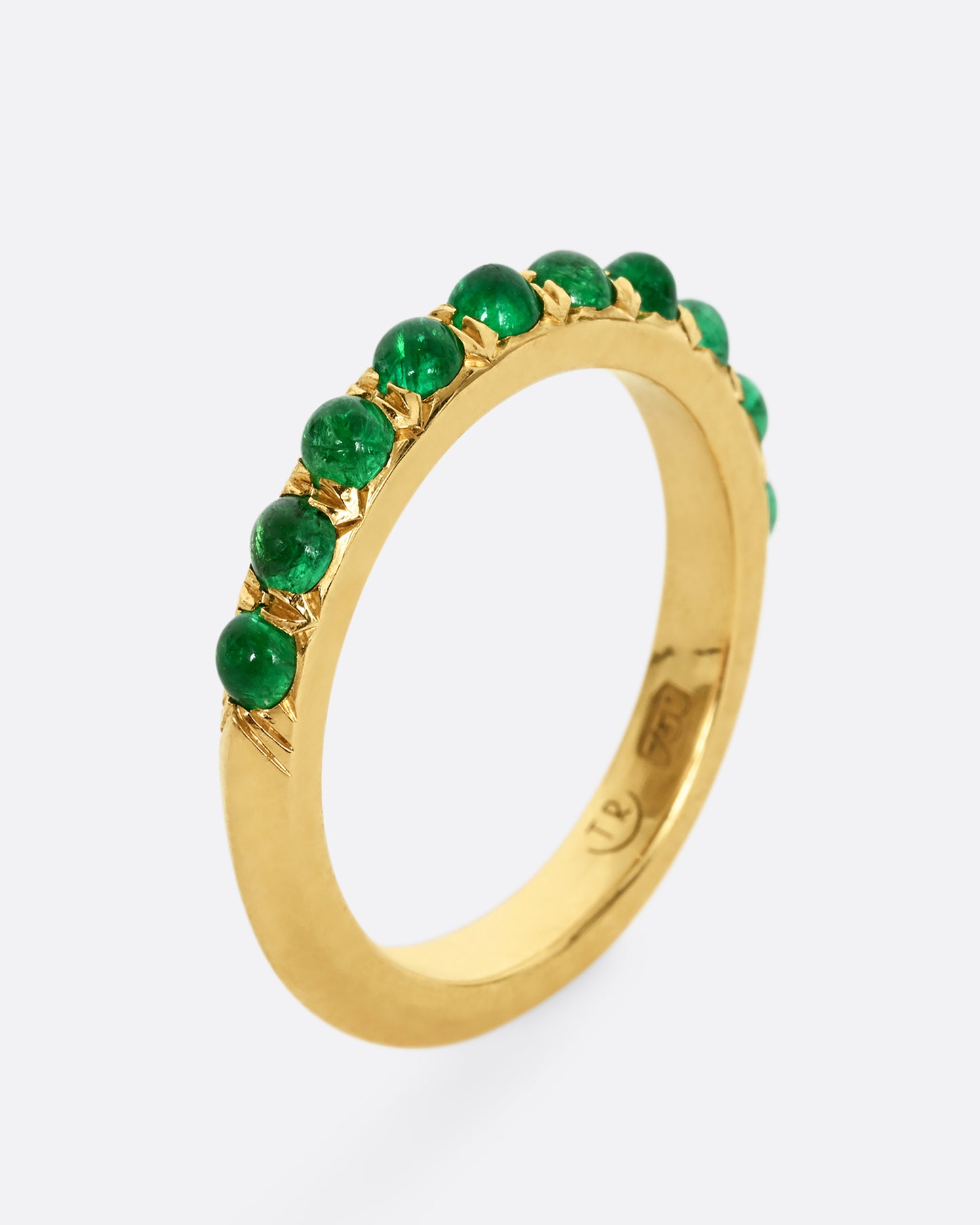 A yellow gold eternity band with emerald cabochons. Shown from the side, standing up.