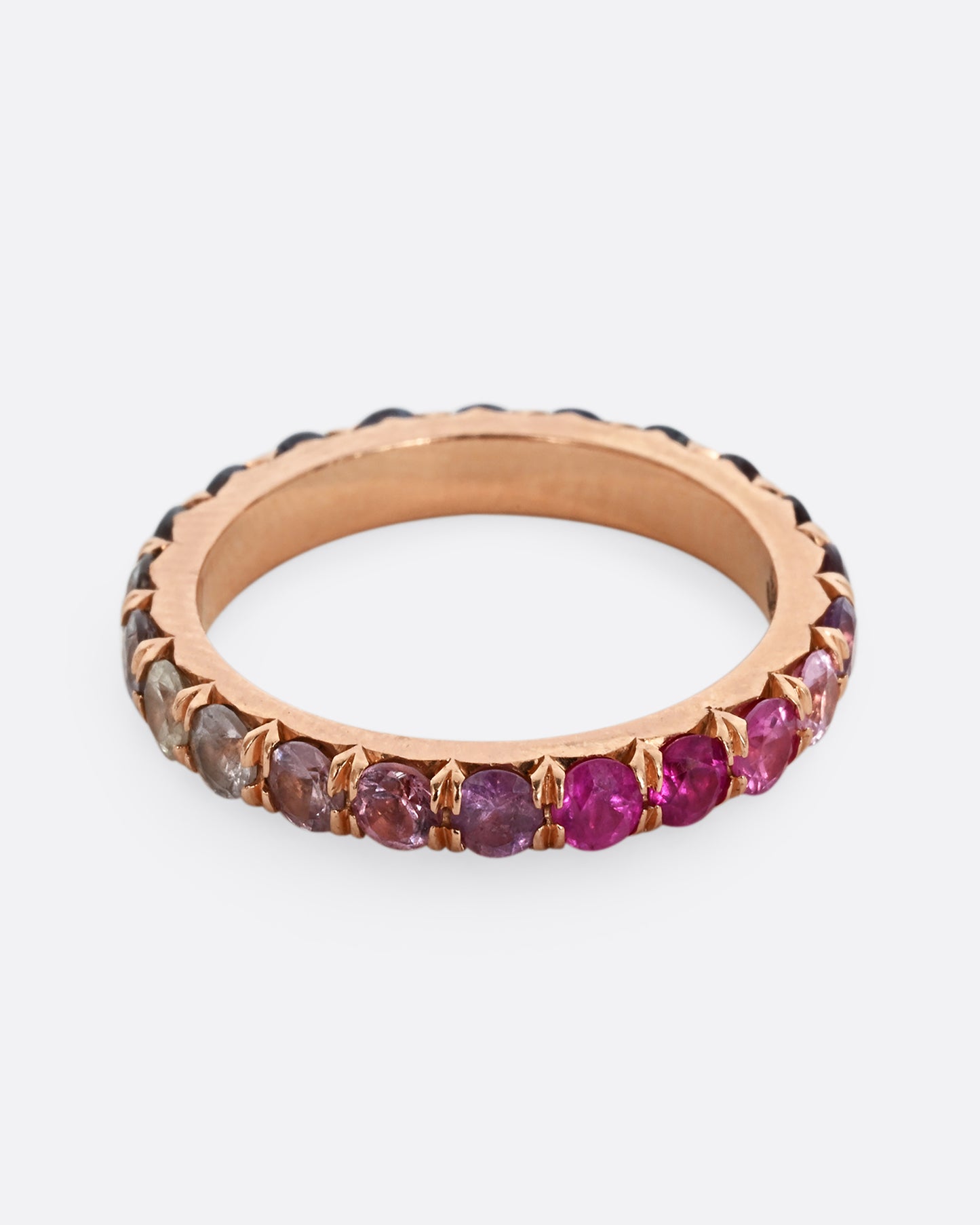 A rose gold eternity band with pink and blue cut sapphires.