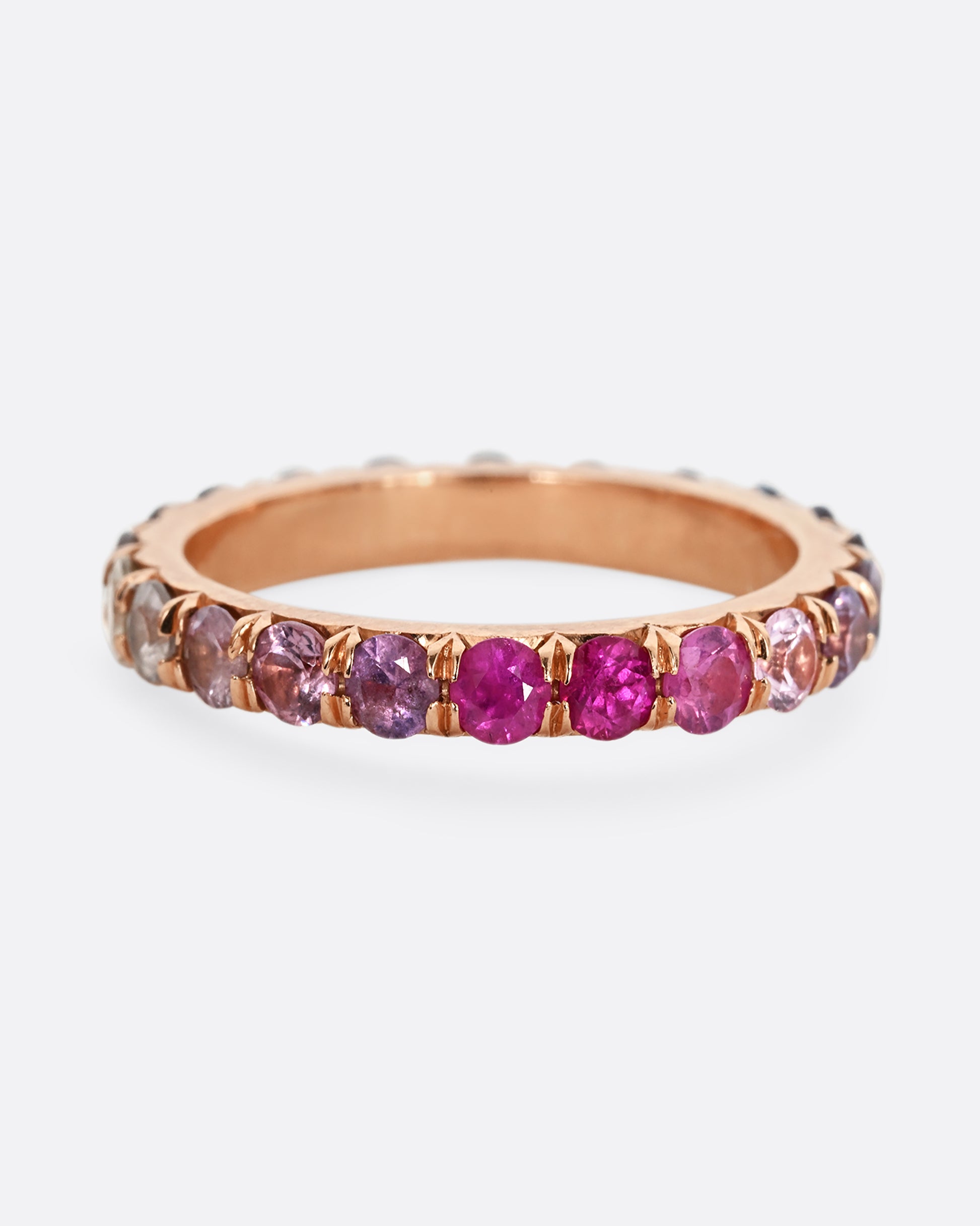 A rose gold eternity band with pink and blue cut sapphires.