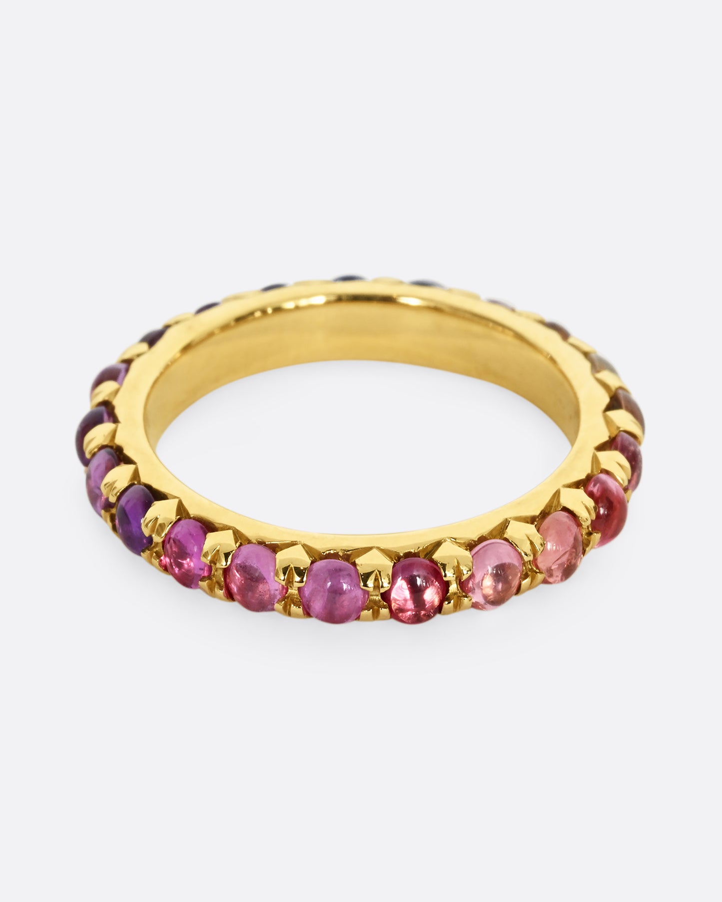 A yellow gold eternity band with pink and purple sapphire cabochons. 