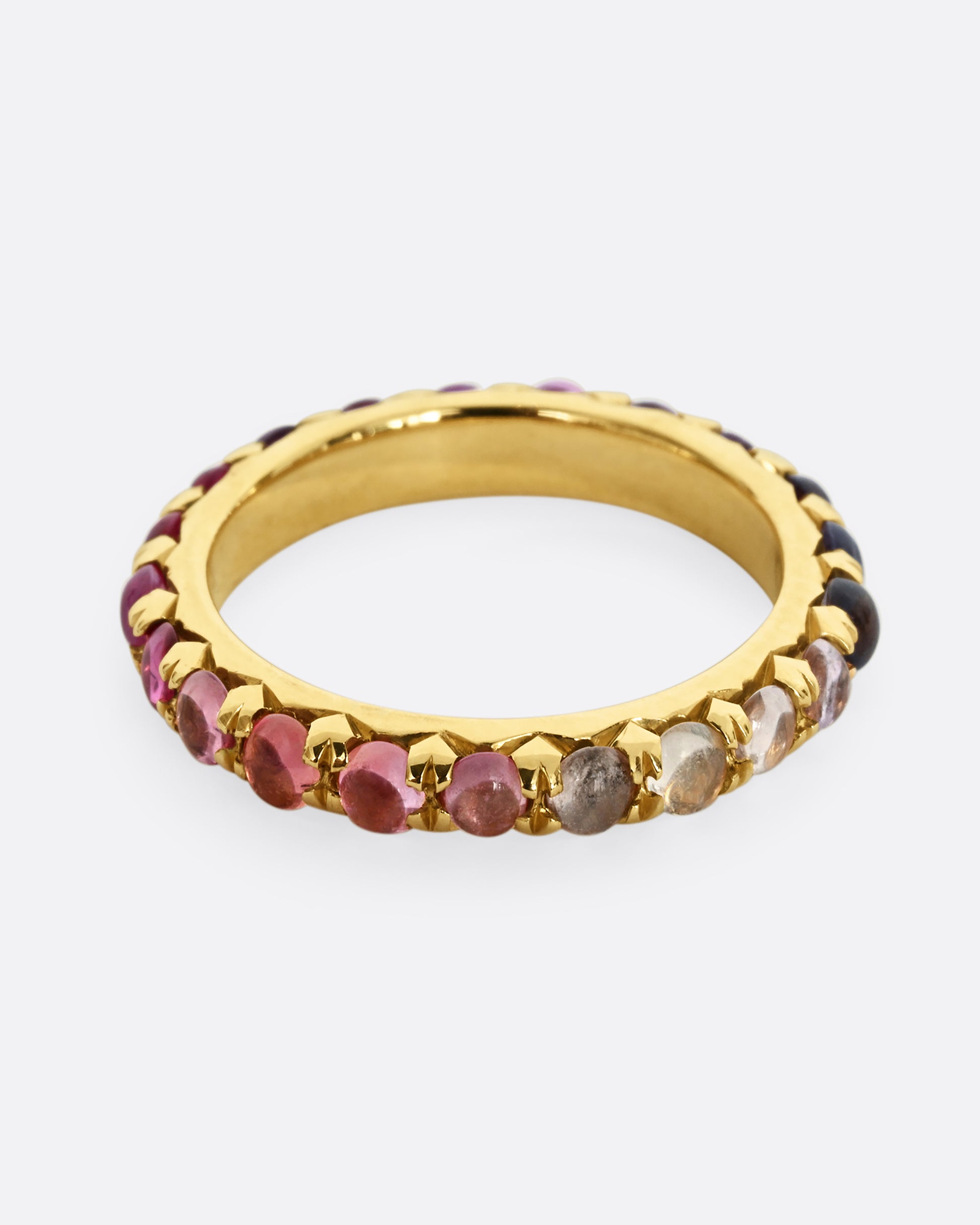 A yellow gold eternity band with pink and purple sapphire cabochons. 