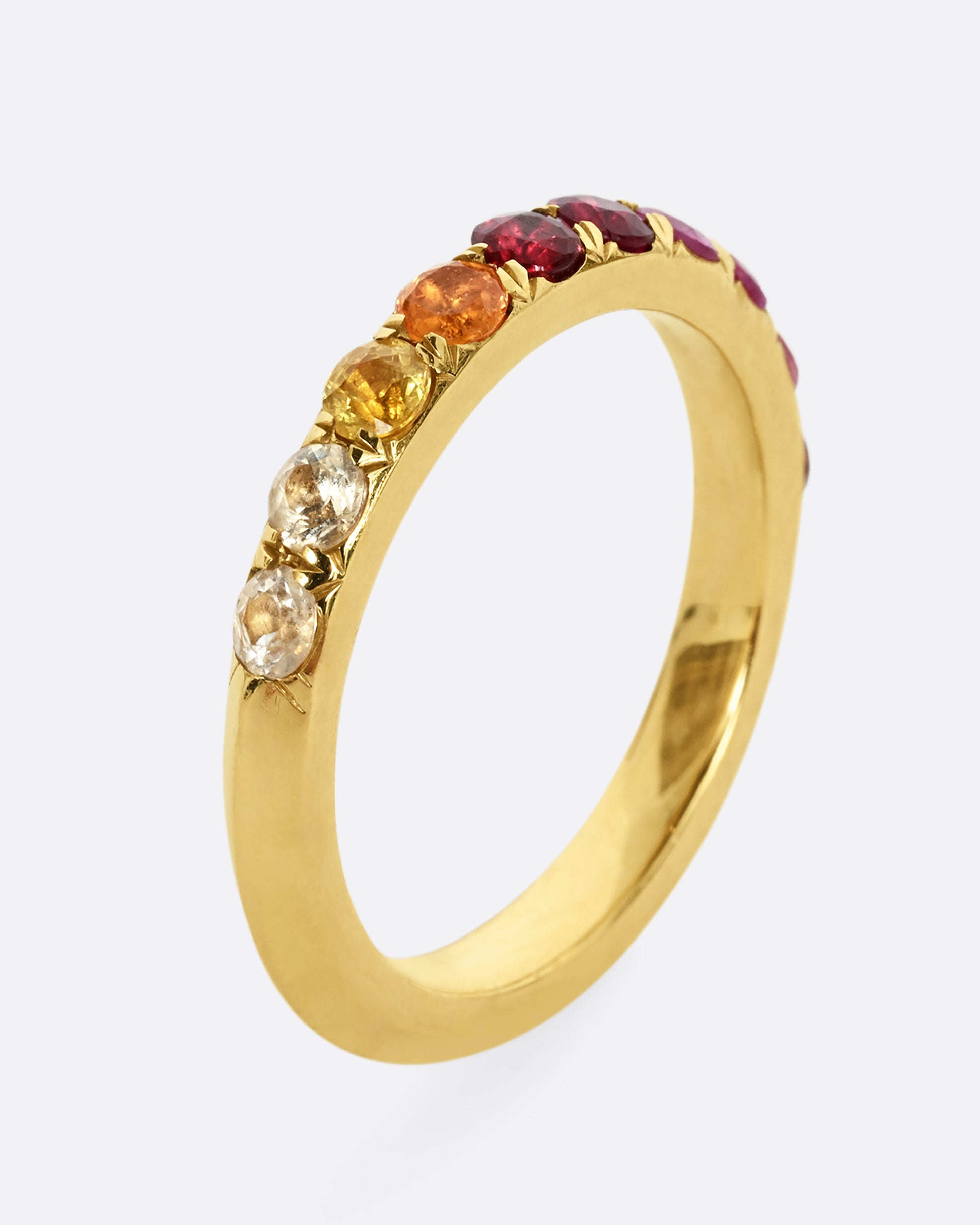 A yellow gold half eternity band with gradient orange red and pink cut sapphires. Shown from the side, standing up.