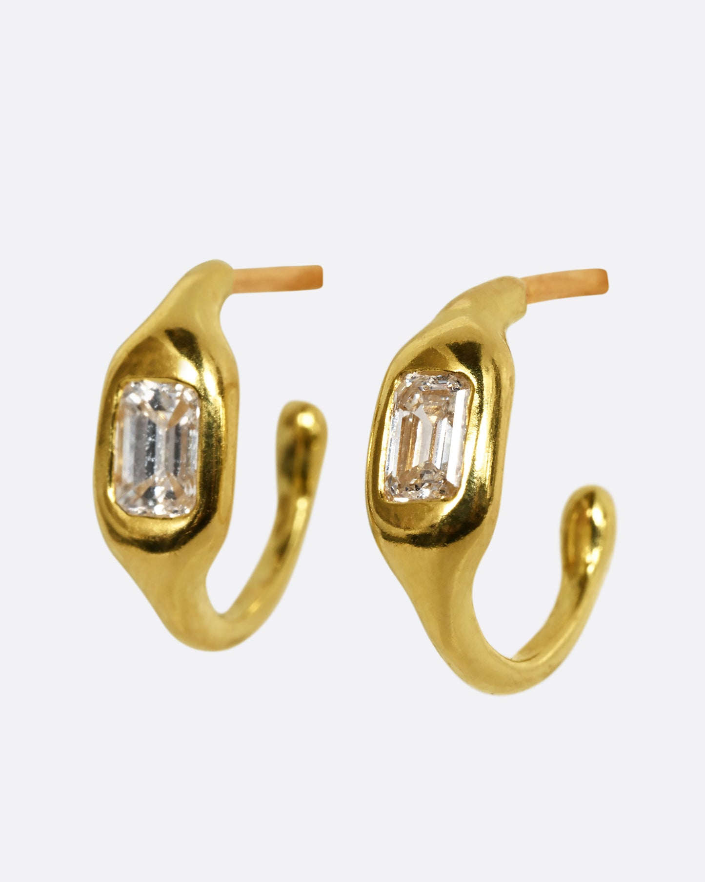 A yellow gold hoop with a single baguette diamond. Shown from the side, with another.