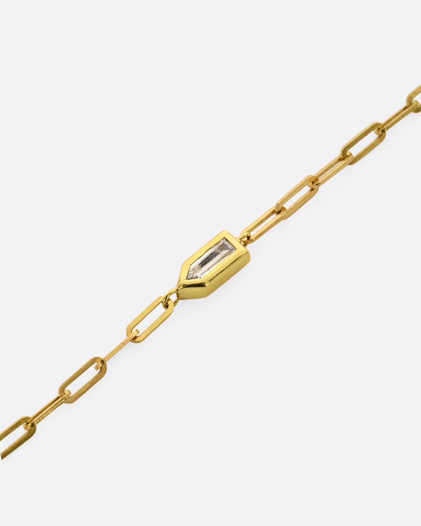 A yellow gold paperclip chain bracelet with a bullet shaped diamond channel. Shown up close.