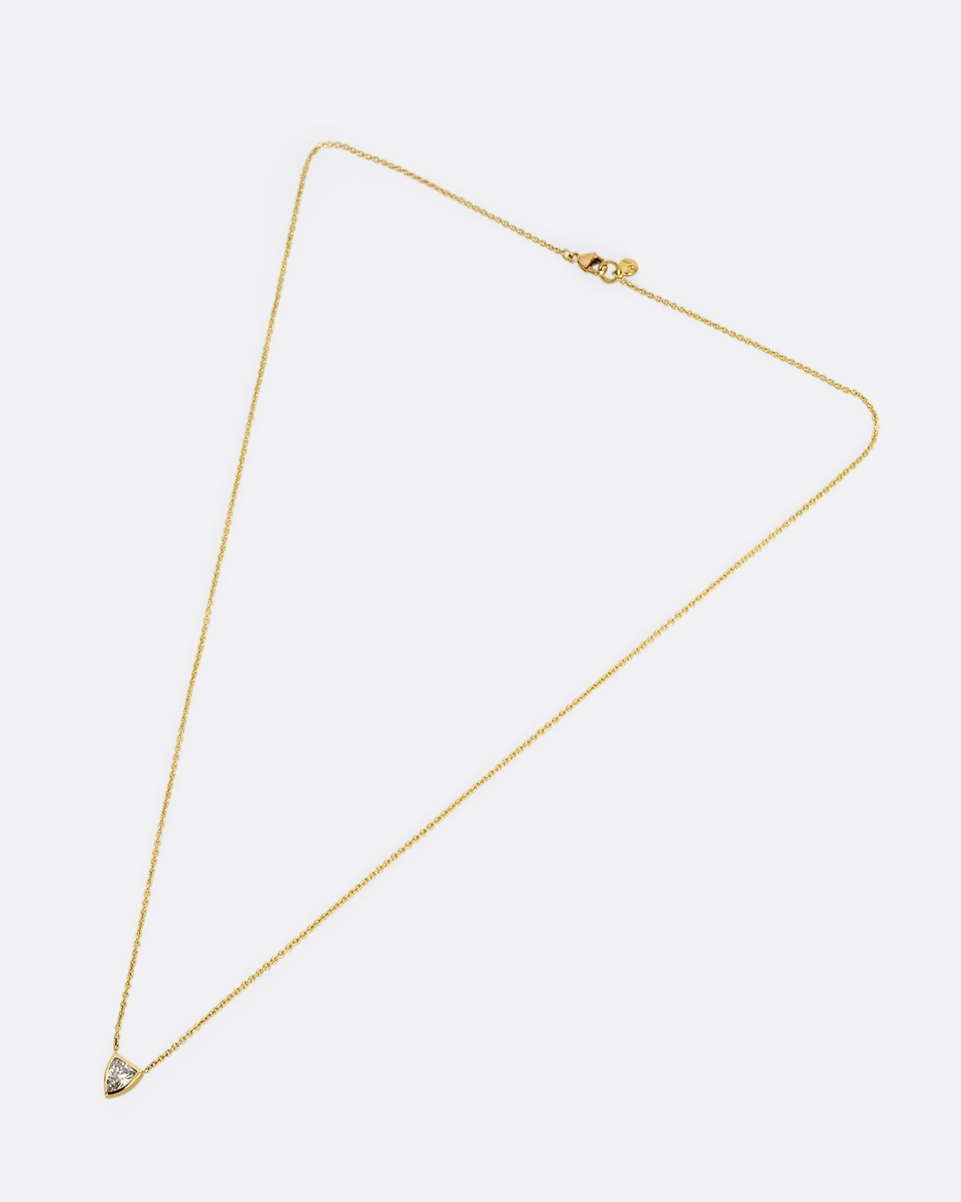 A yellow gold necklace with a shield shaped diamond. Shown laying flat.