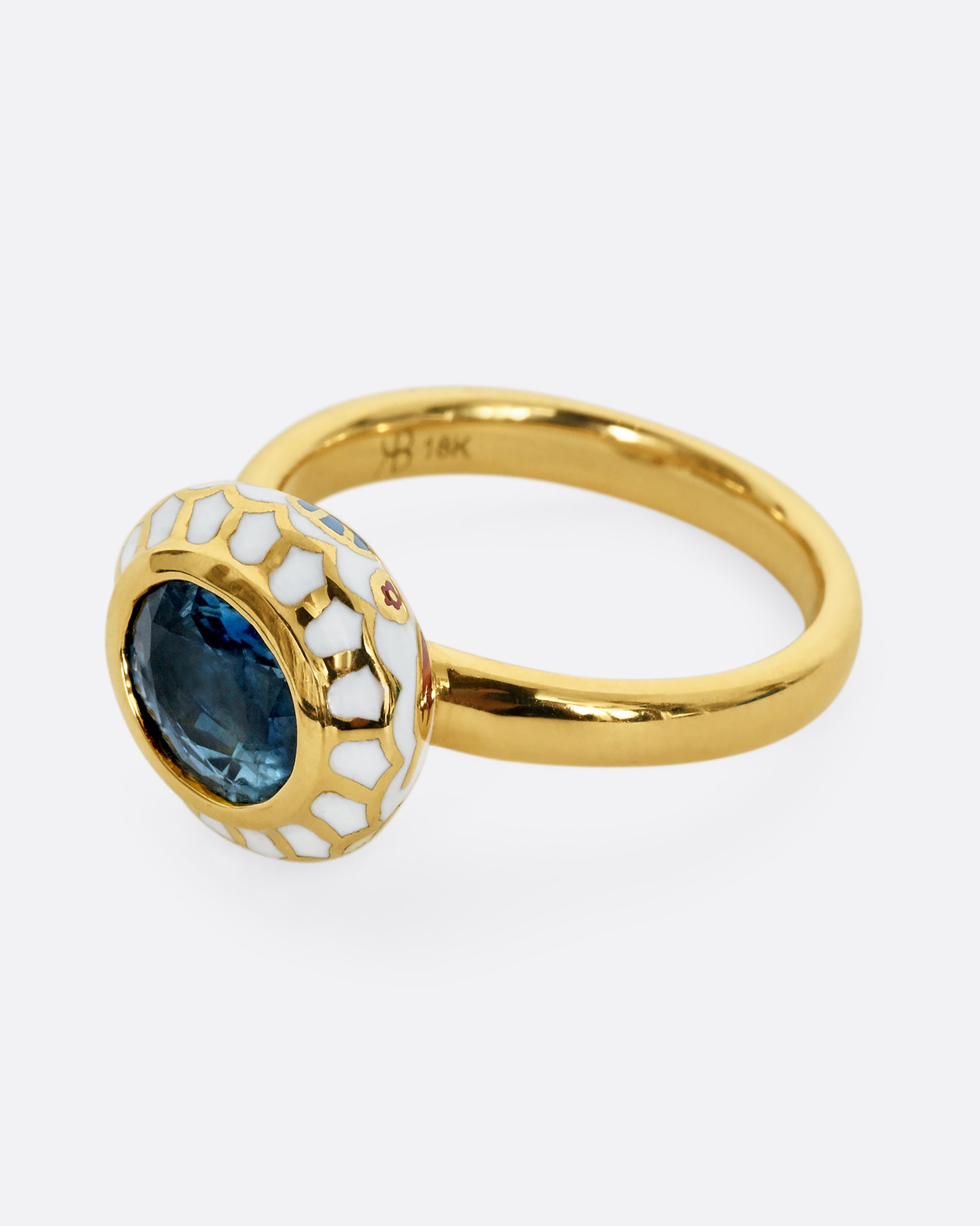 A yellow gold ring with a light blue sapphire and white enamel halo. Shown from the side.