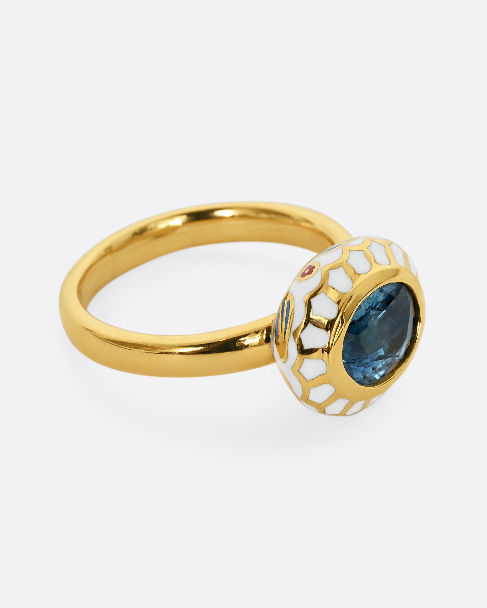 A yellow gold ring with a light blue sapphire and white enamel halo. Shown from the side.