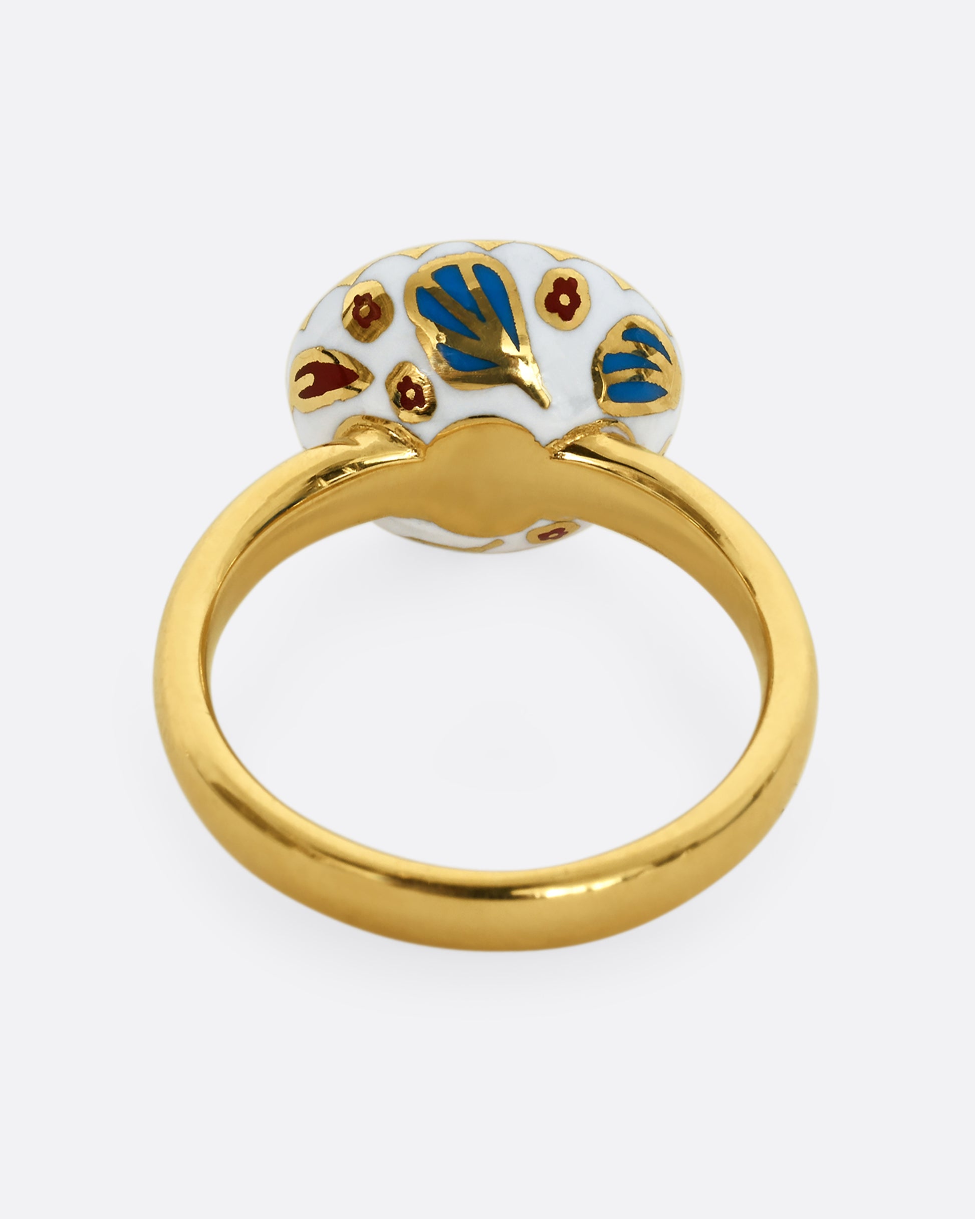 A yellow gold ring with a light blue sapphire and white enamel halo. Shown from the back.