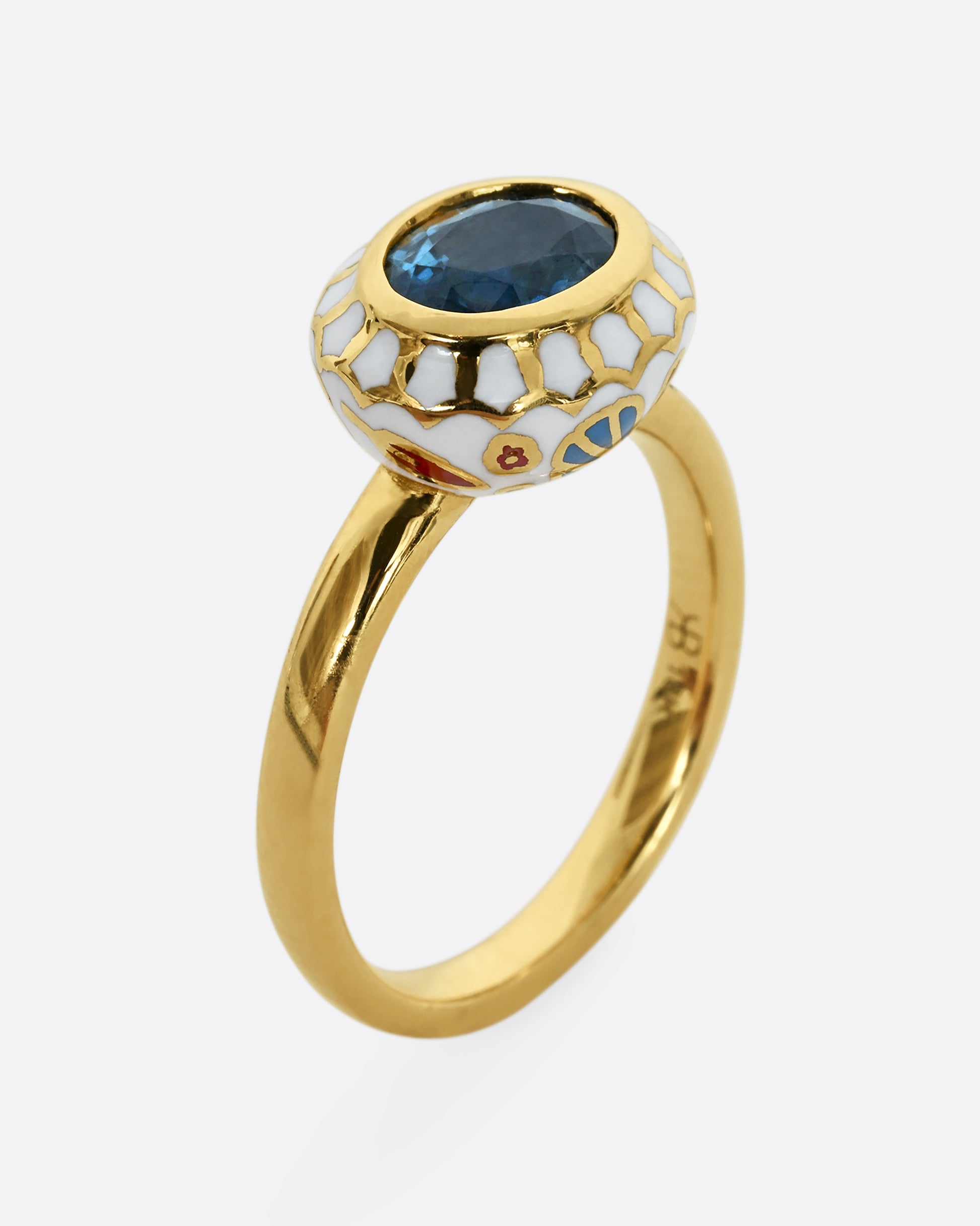 A yellow gold ring with a light blue sapphire and white enamel halo. Shown from the side, close up.