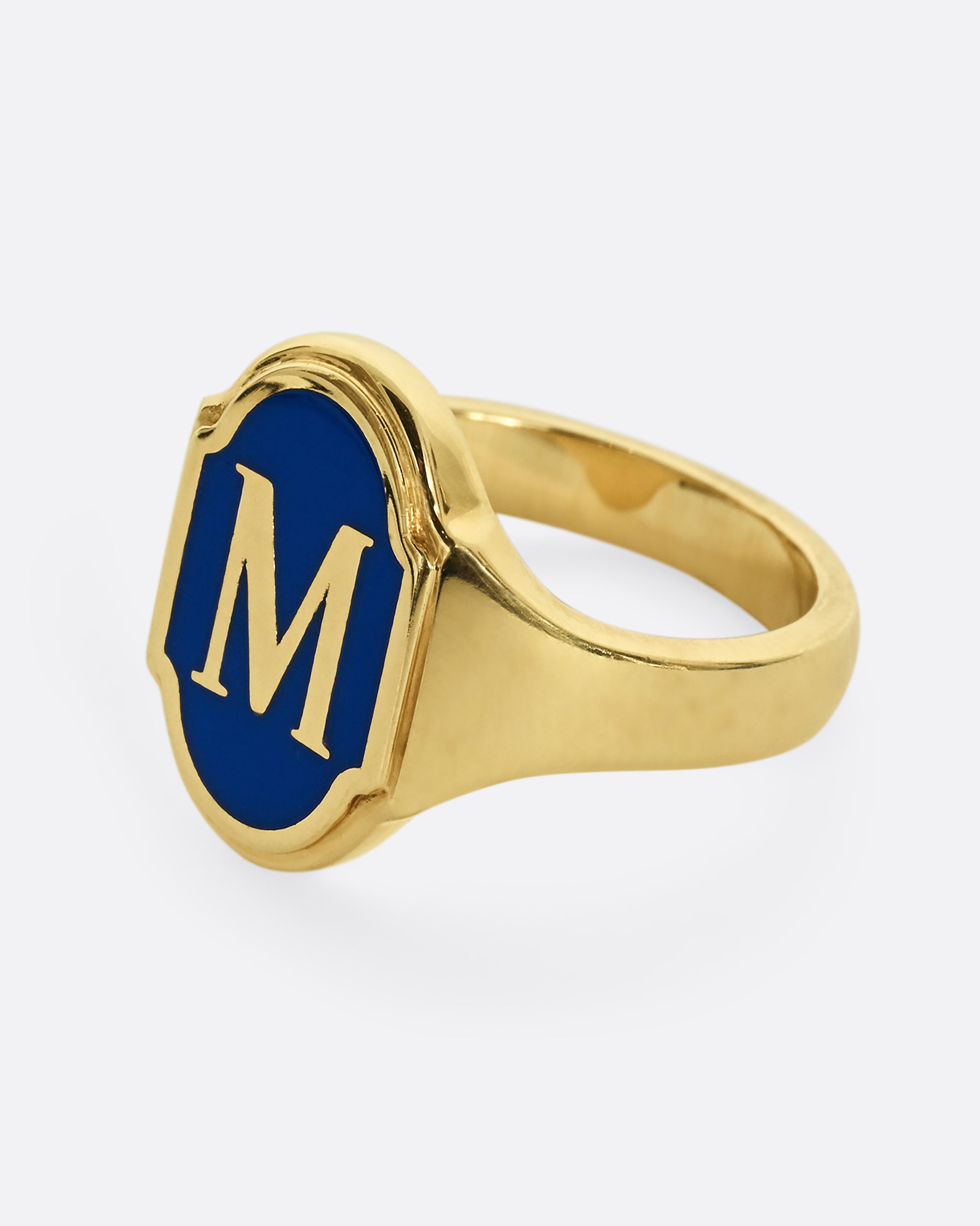 A yellow gold signet ring with blue enamel and the letter "M". Shown from the side.