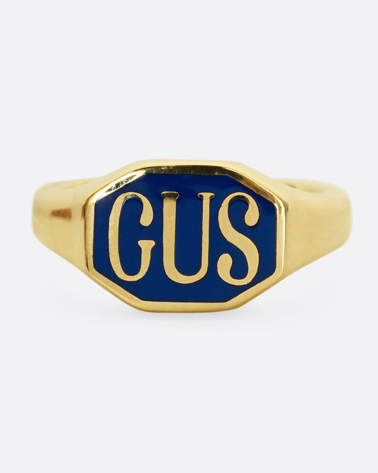 A yellow gold signet ring with the initials "GUS" and blue enamel. Shown from the front.