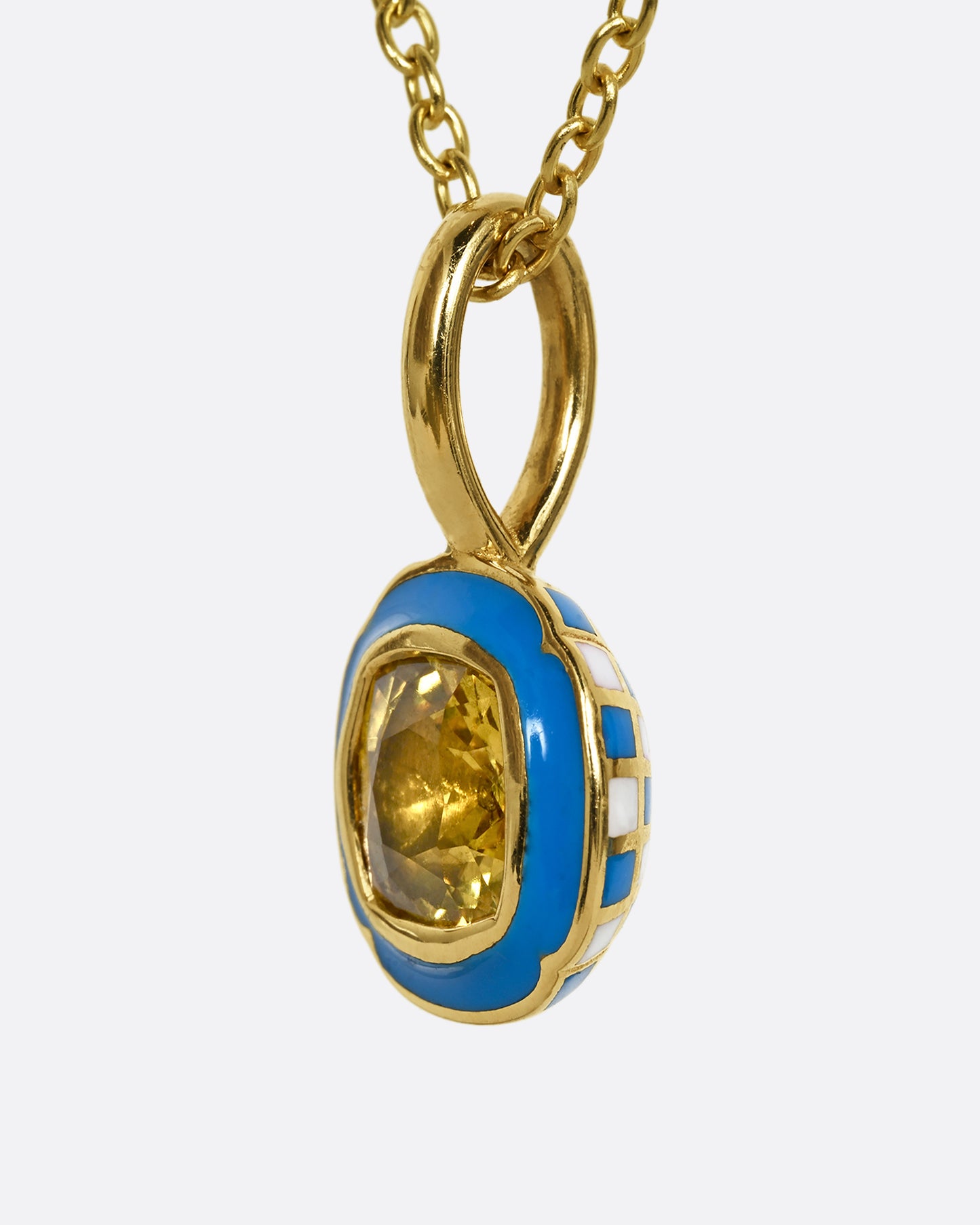 A yellow gold pendant with blue enamel surrounding a cushion cut yellow sapphire. Shown from the side.