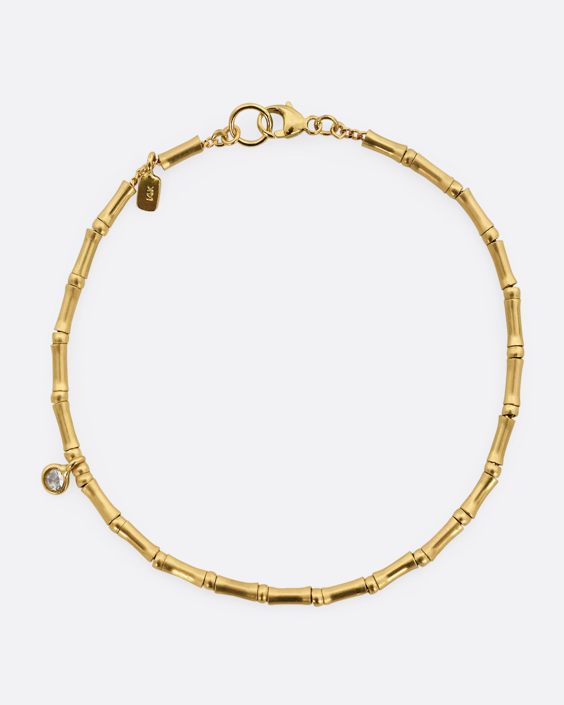 A yellow gold bracelet with tube beads and a single diamond. Shown from above.