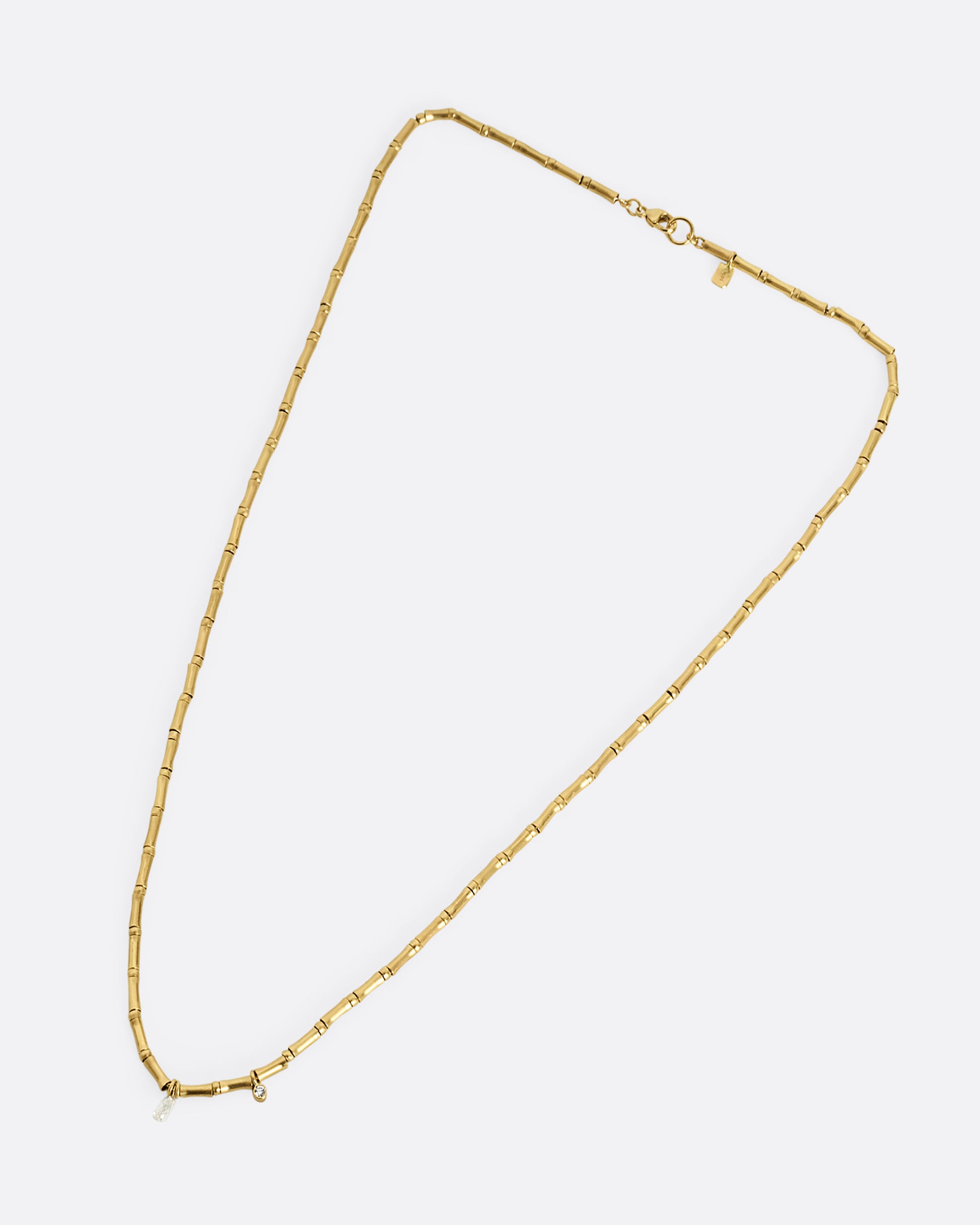 A yellow gold tube beaded necklace with two diamonds. Shown laying flat.