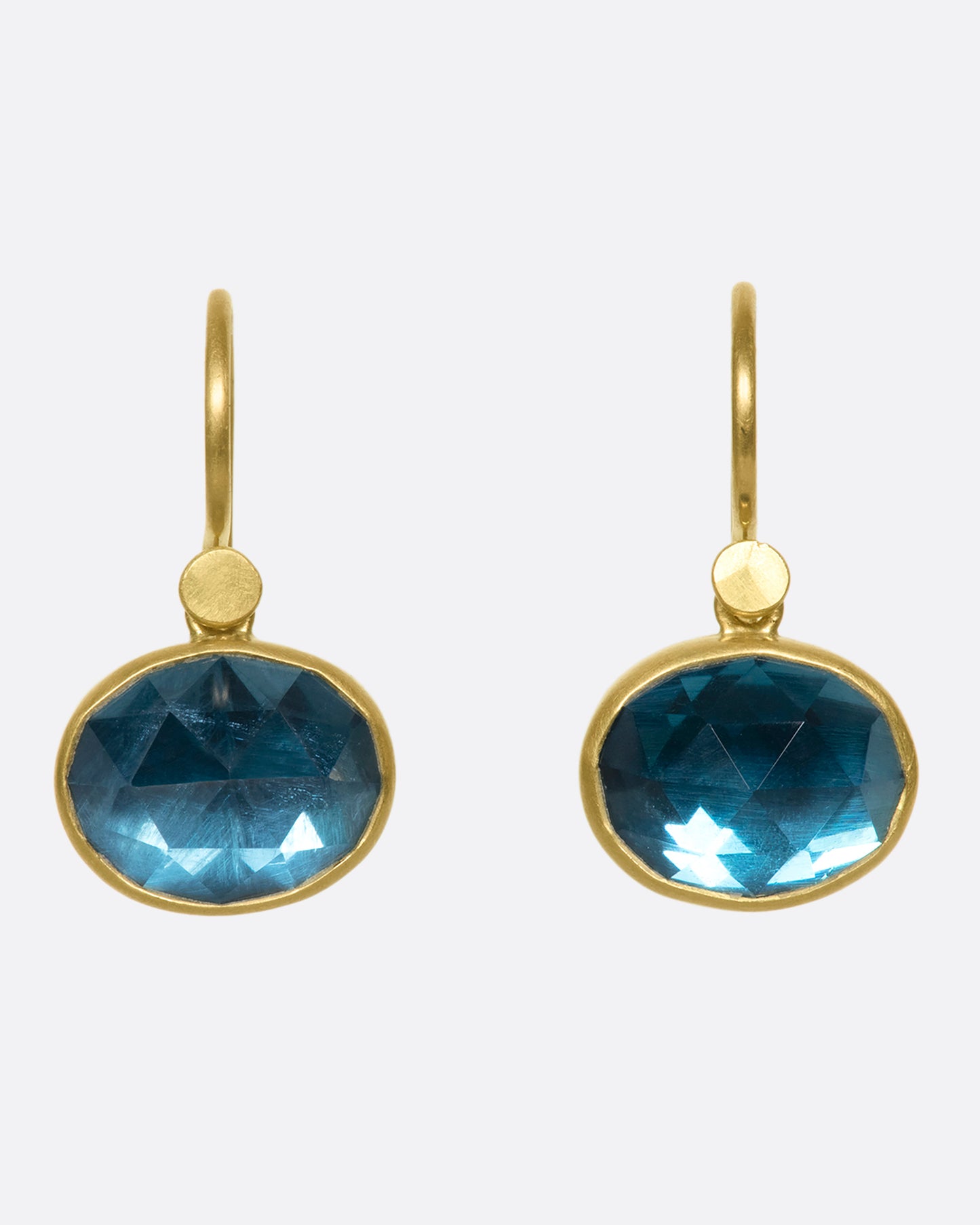 18k gold dangling earrings with oval London blue topaz drops. The rich blue topaz looks like sunlit water wrapped in a gold bezel setting.