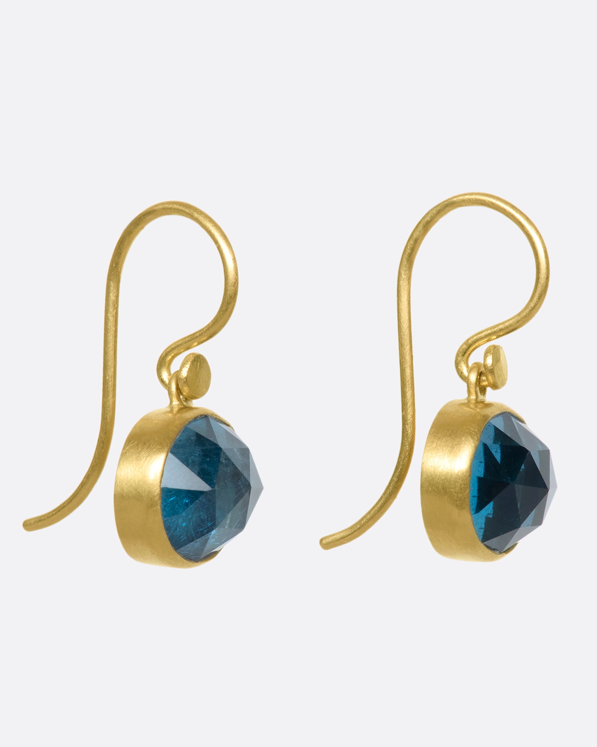 18k gold dangling earrings with oval London blue topaz drops. The rich blue topaz looks like sunlit water wrapped in a gold bezel setting.