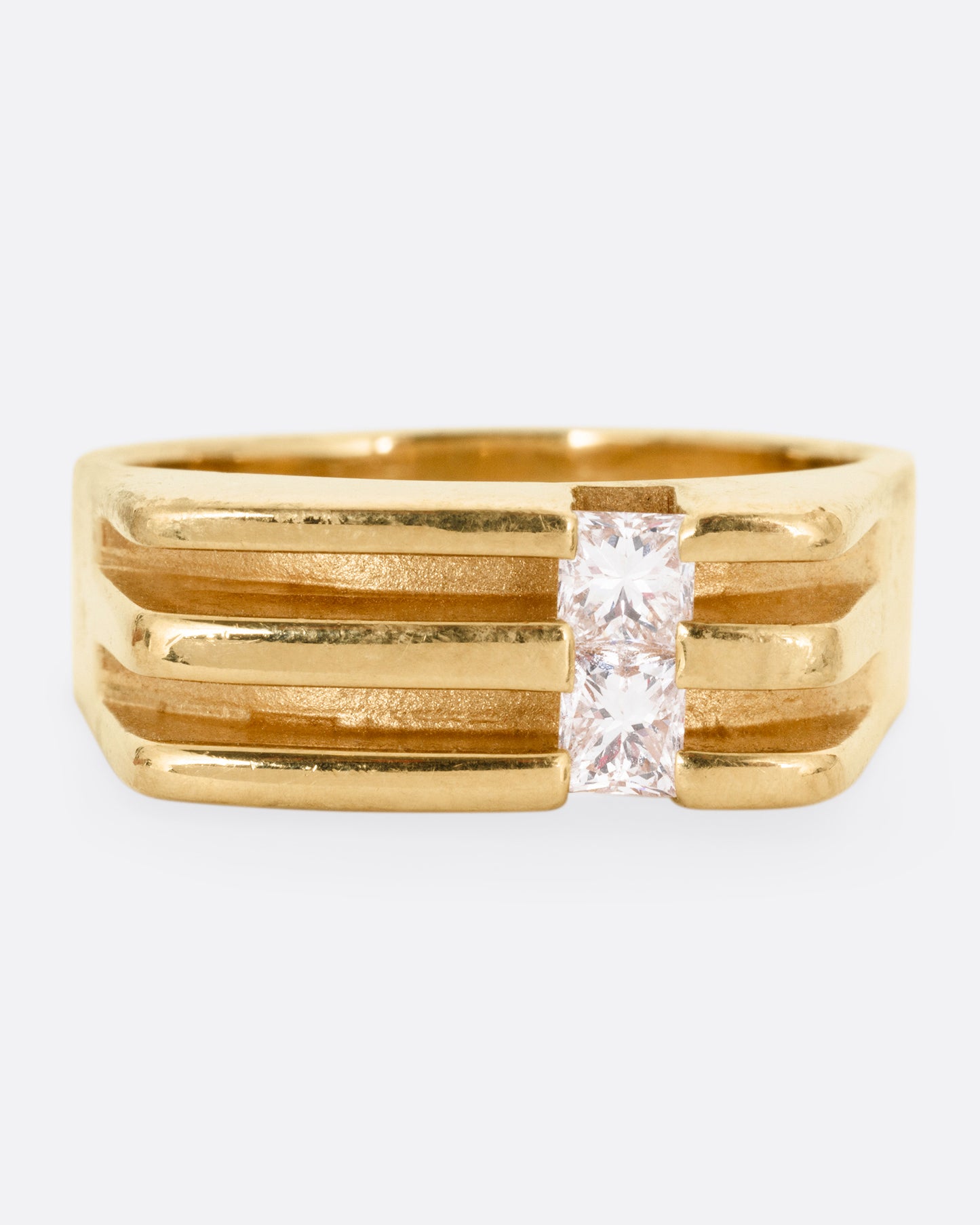 A yellow gold ring with linear channels and two princess cut diamonds, shown from the front. 