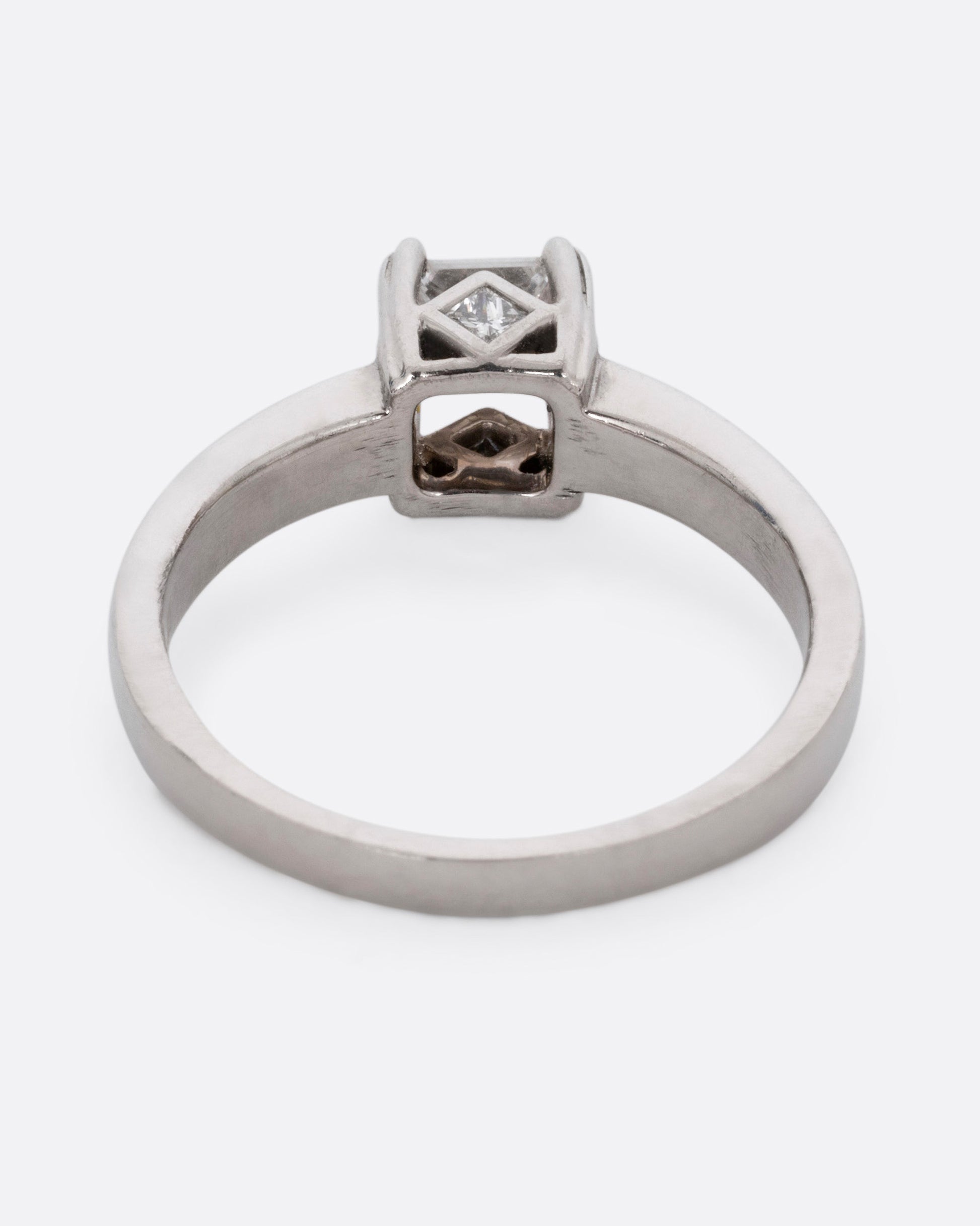 A platinum ring with a princess cut diamond, prong set high above angular cutouts and diamond accents. Shown from the back.