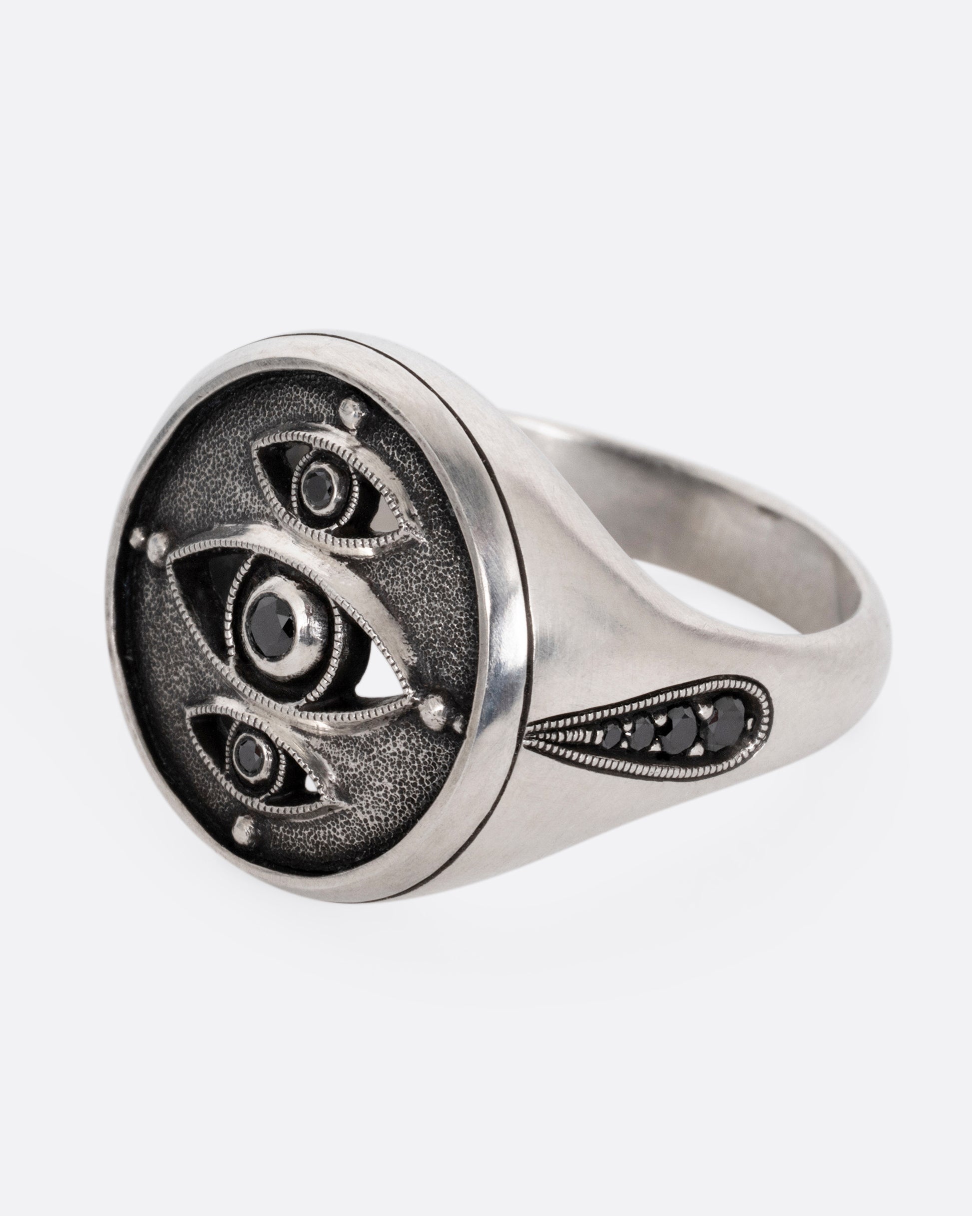 A silver ring with three eyes with black diamond centers, shown from the side.