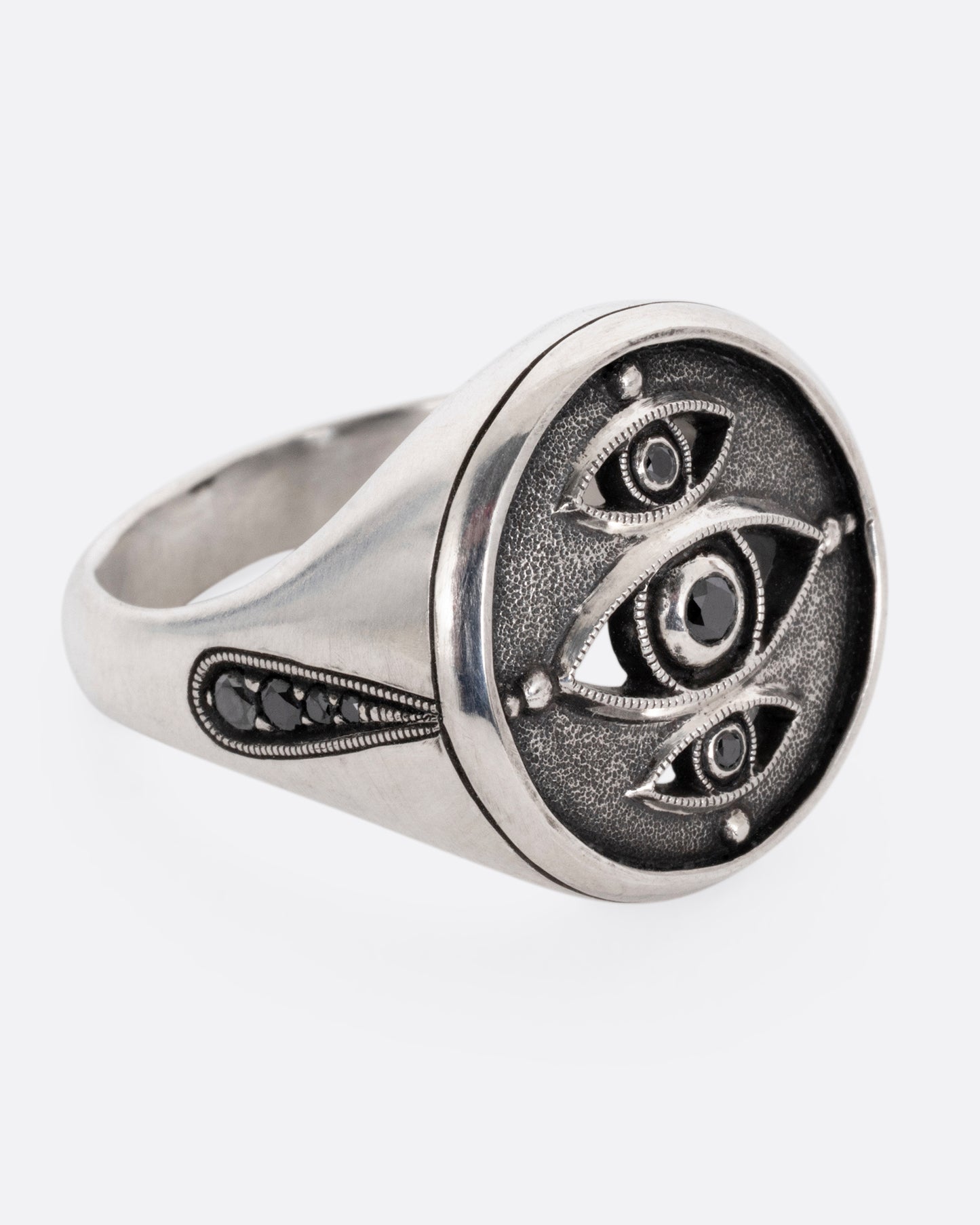 A silver ring with three eyes with black diamond centers, shown from the side.