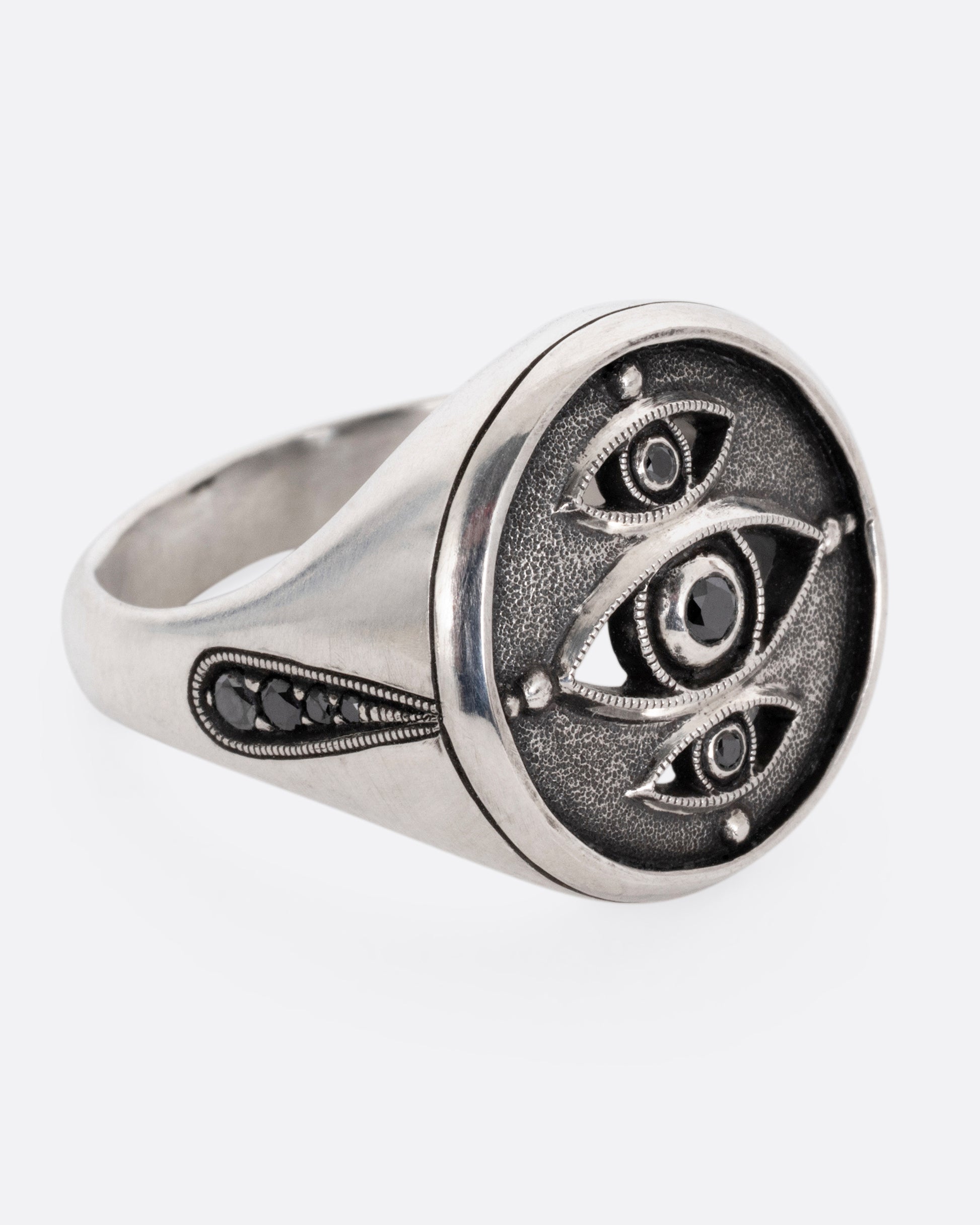 A silver ring with three eyes with black diamond centers, shown from the side.