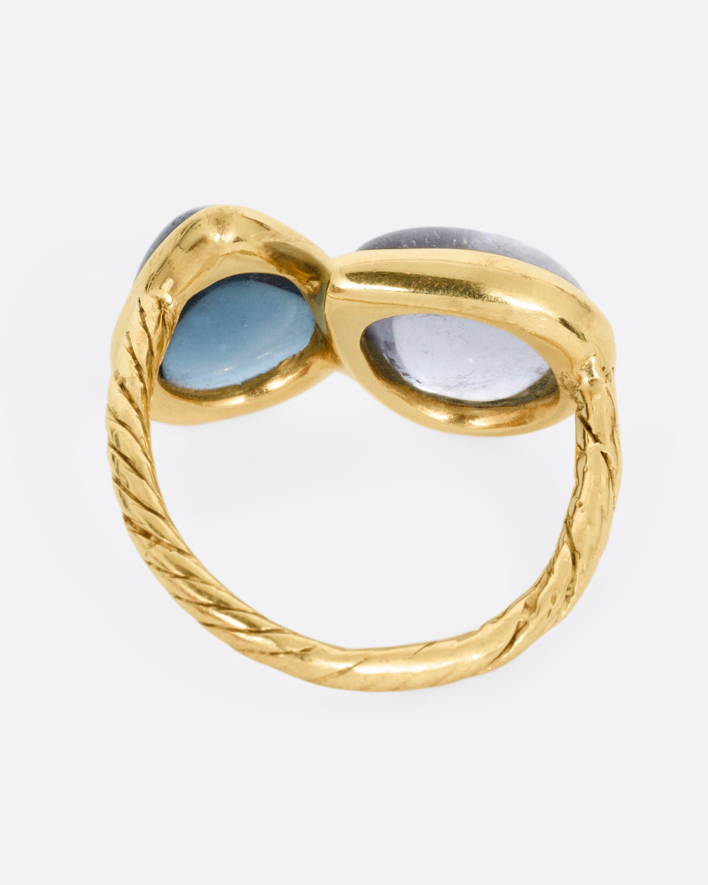A yellow gold ring with a pair of blue green tourmalines and a textured hand- carved band, shown from the back.