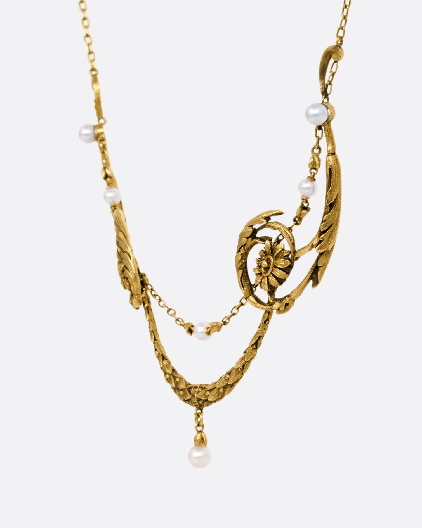 A yellow gold necklace with pearls and flower details, shown from the side.
