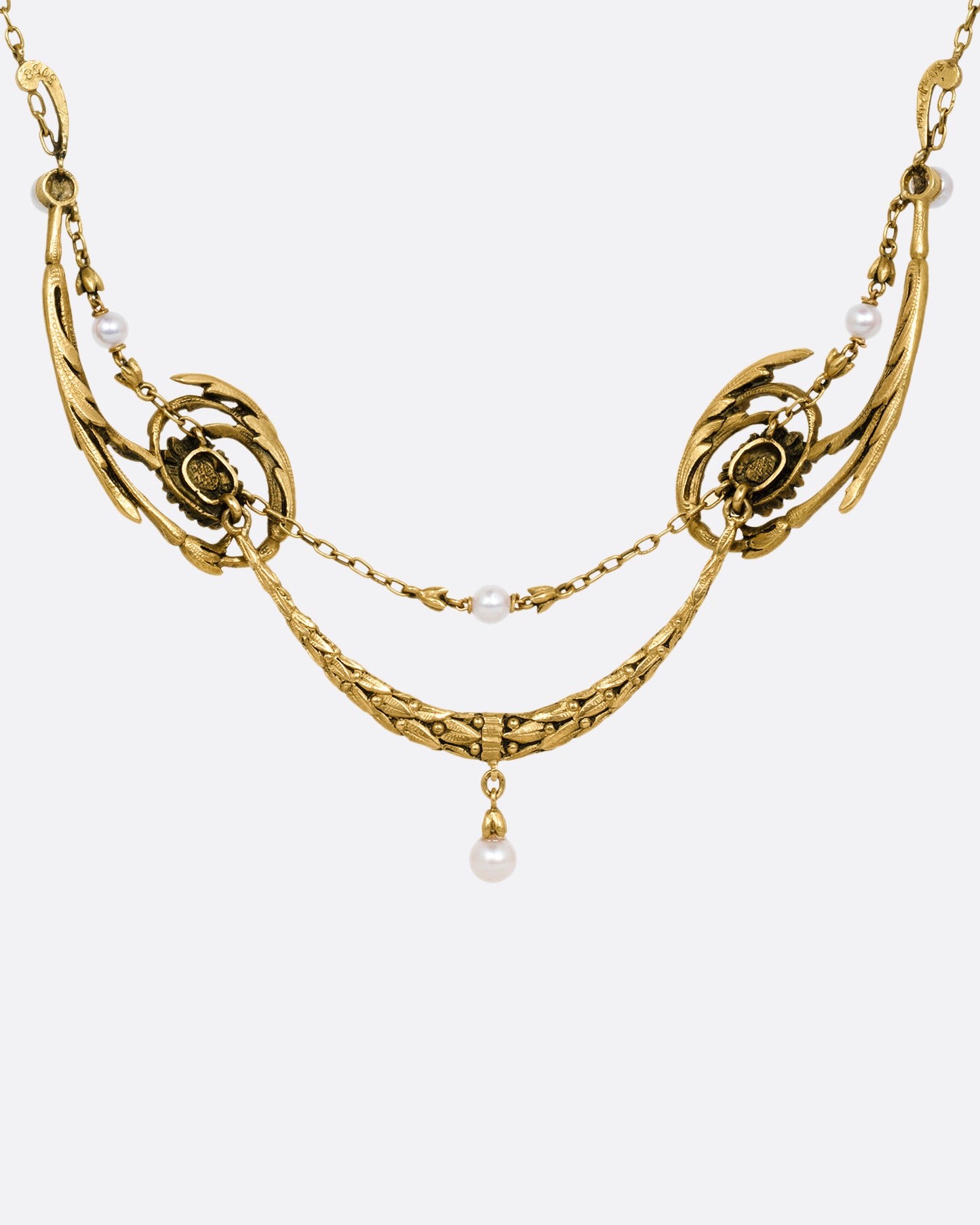 A yellow gold necklace with pearls and flower details, shown from the back.