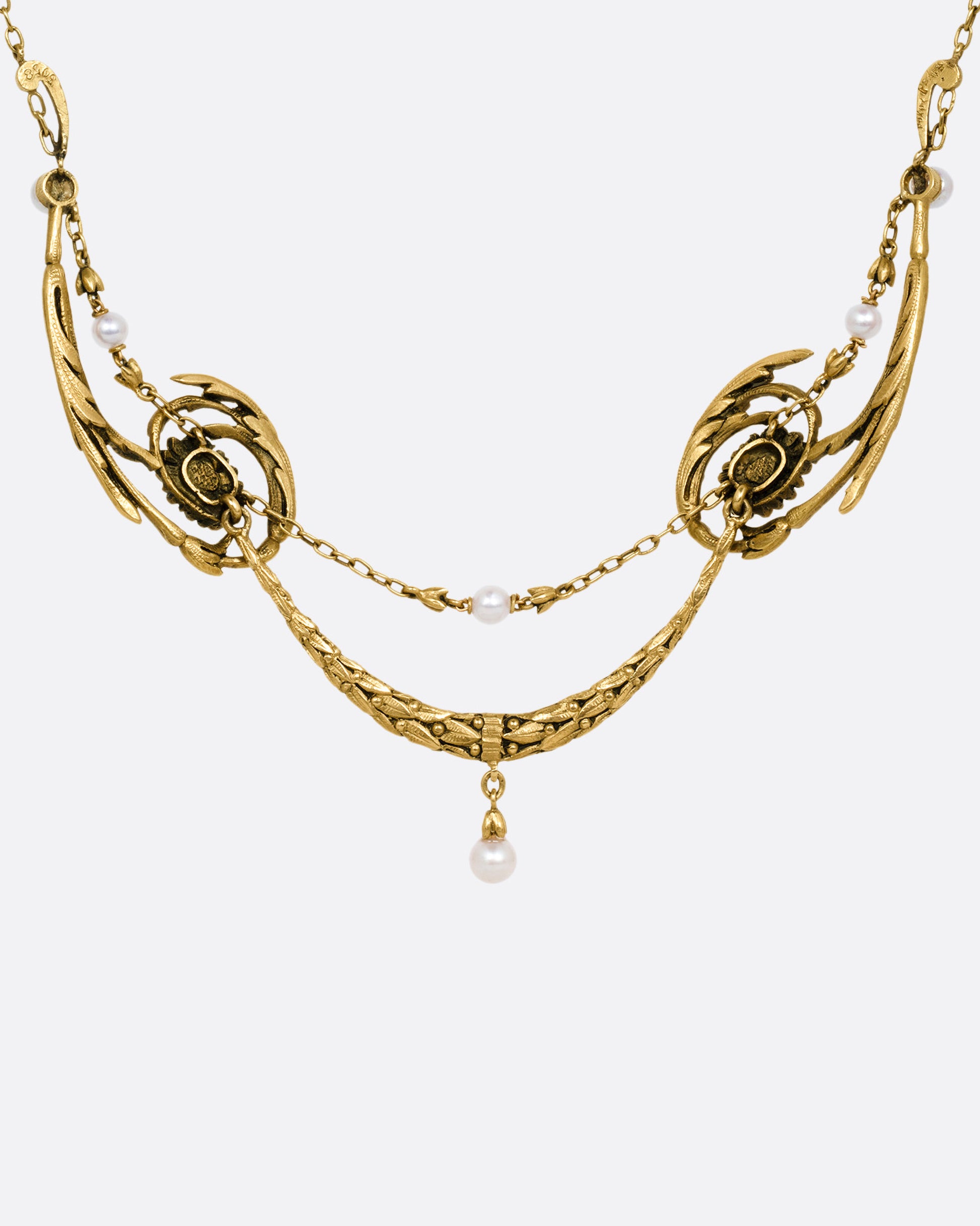 A yellow gold necklace with pearls and flower details, shown from the back.