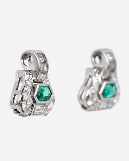 A pair of platinum earrings with emeralds and diamonds, shown from the side.