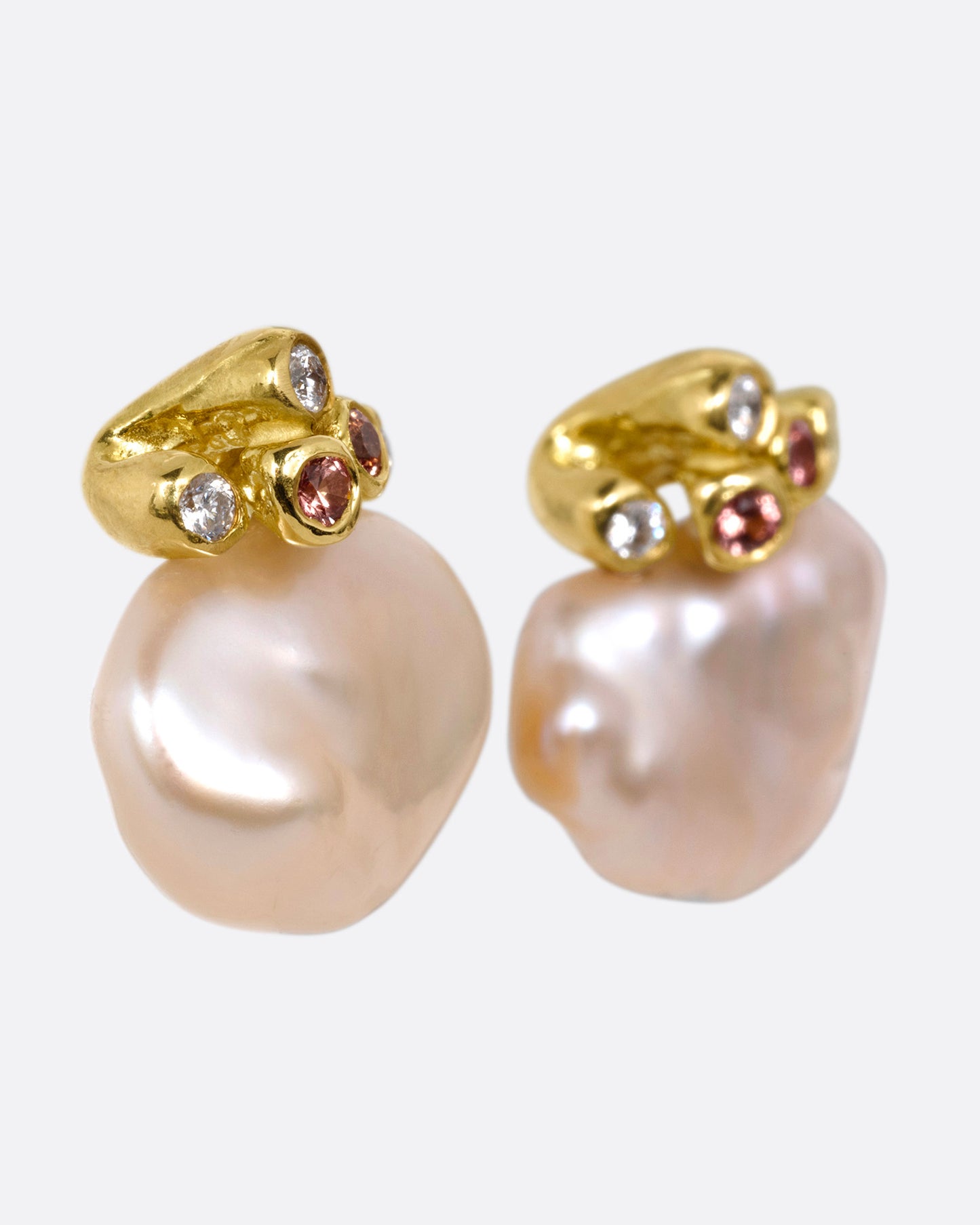 A pair of yellow gold stud earrings with diamond and orange sapphire clusters atop two pink freeform Keshi pearls, shown from the side.