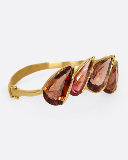 A yellow gold bracelet with five teardrop shaped tourmalines, shown from the side.
