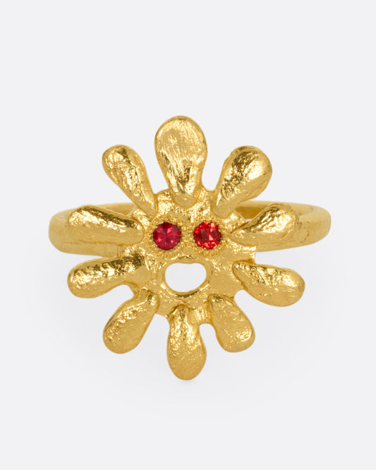 A yellow gold sun shaped ring with red stone eyes, shown from the front.