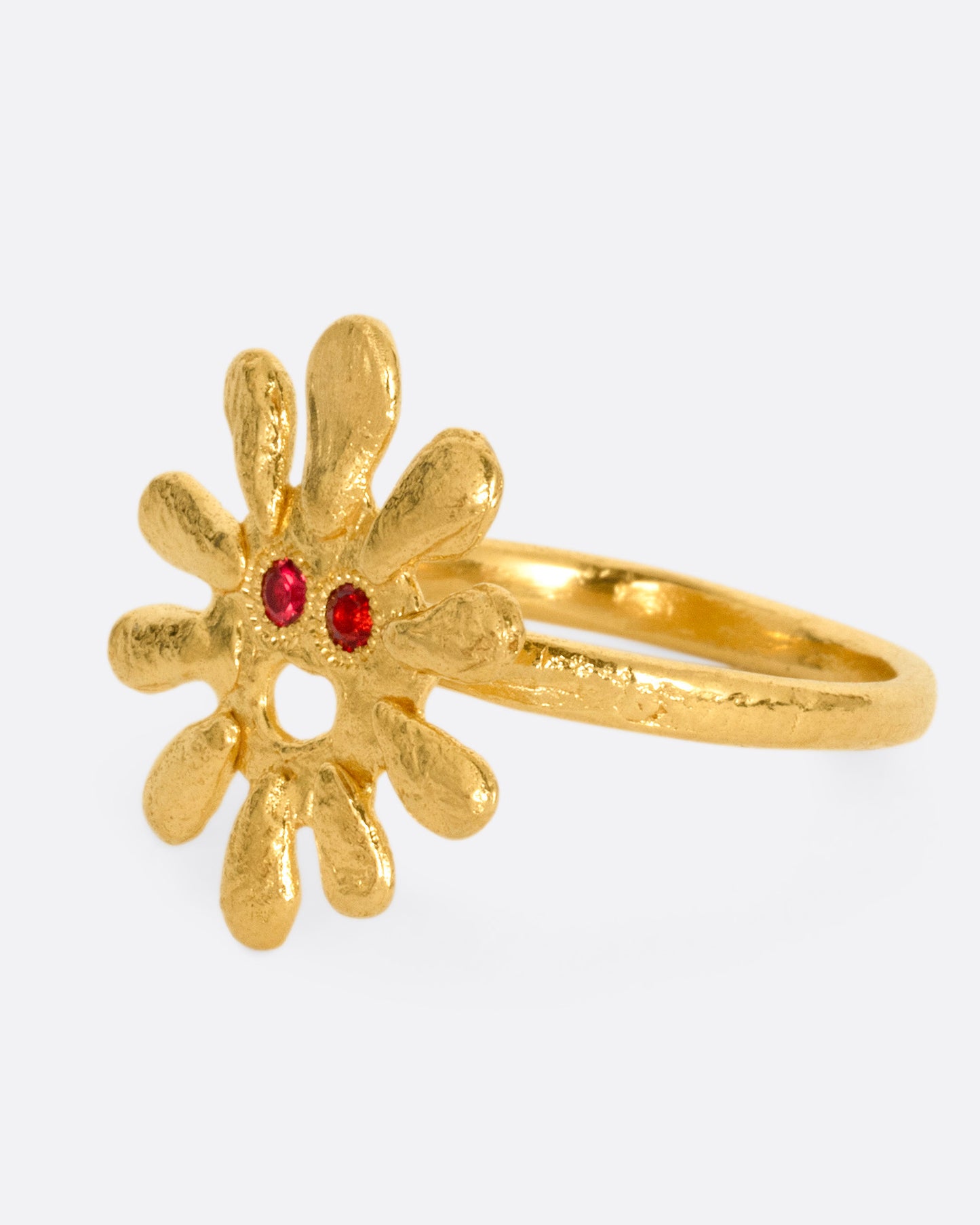 A yellow gold sun shaped ring with red stone eyes, shown from the side.