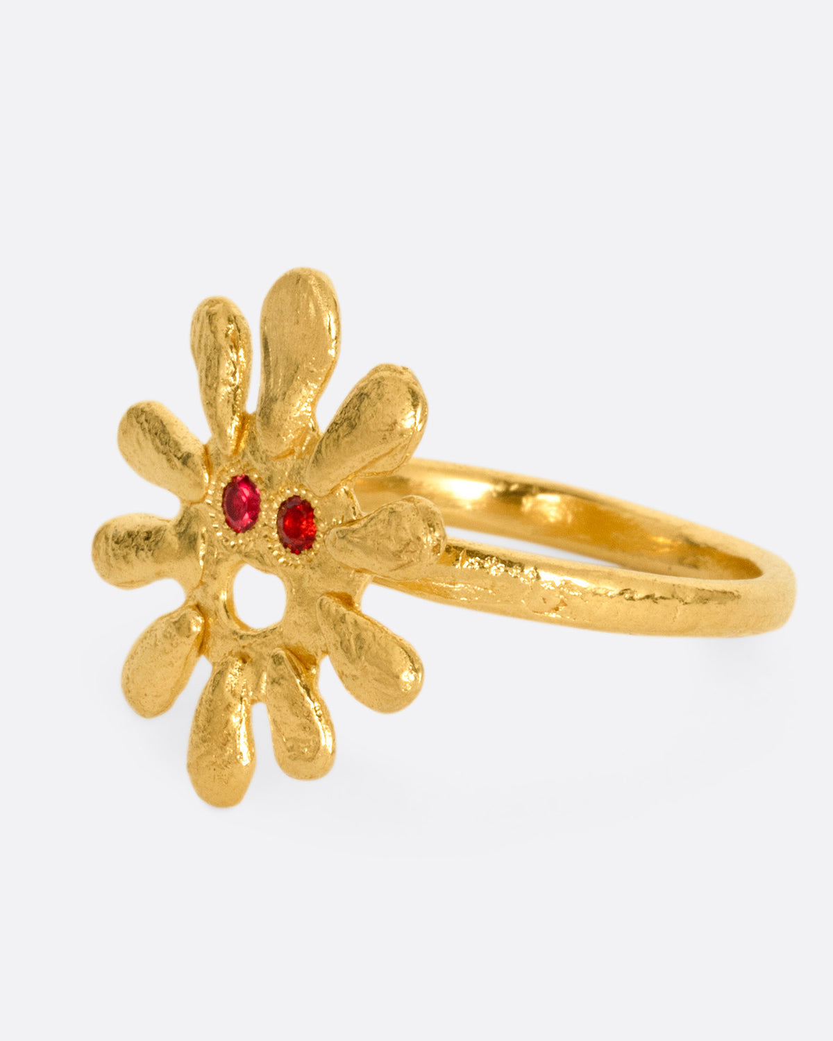 A yellow gold sun shaped ring with red stone eyes, shown from the side.