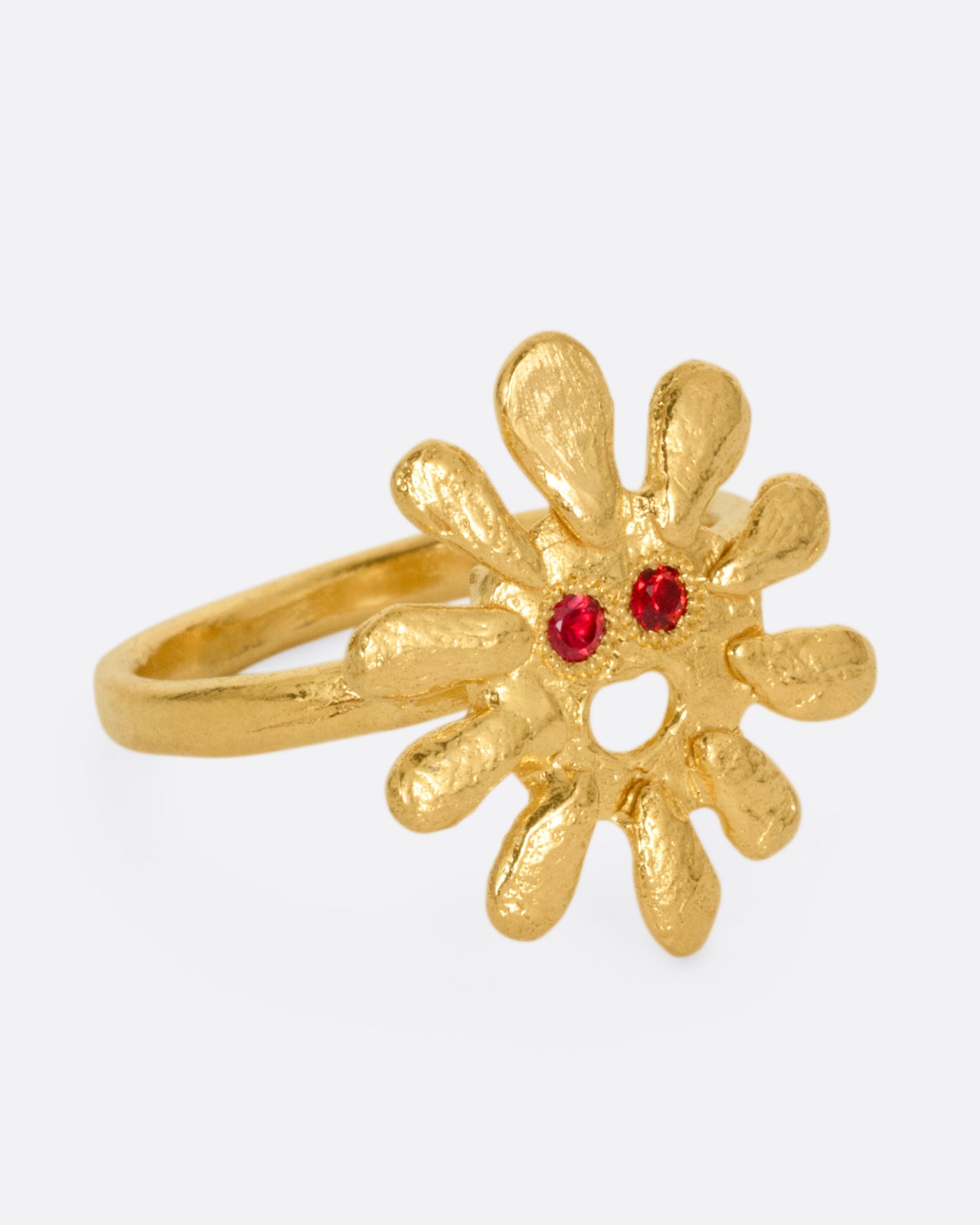A yellow gold sun shaped ring with red stone eyes, shown from the side.
