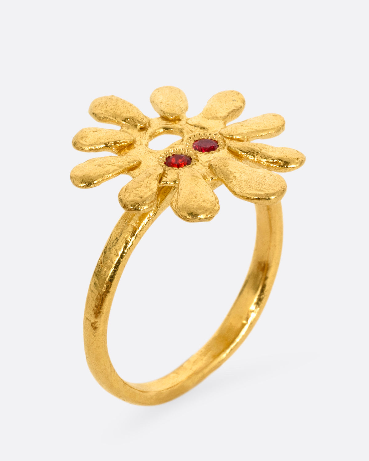 A yellow gold sun shaped ring with red stone eyes, shown standing up from the side.