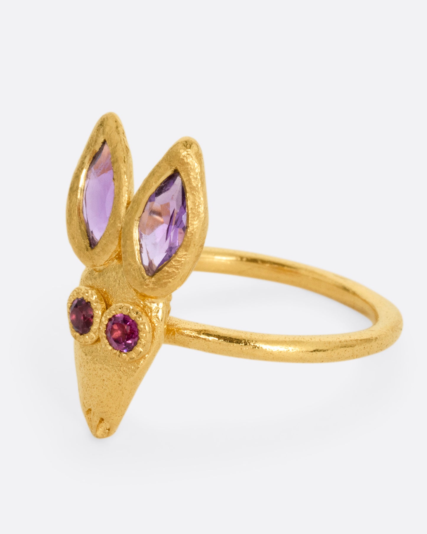 A yellow gold ring with a rabbit face with amethyst ears and tourmaline eyes. Shown from the side.