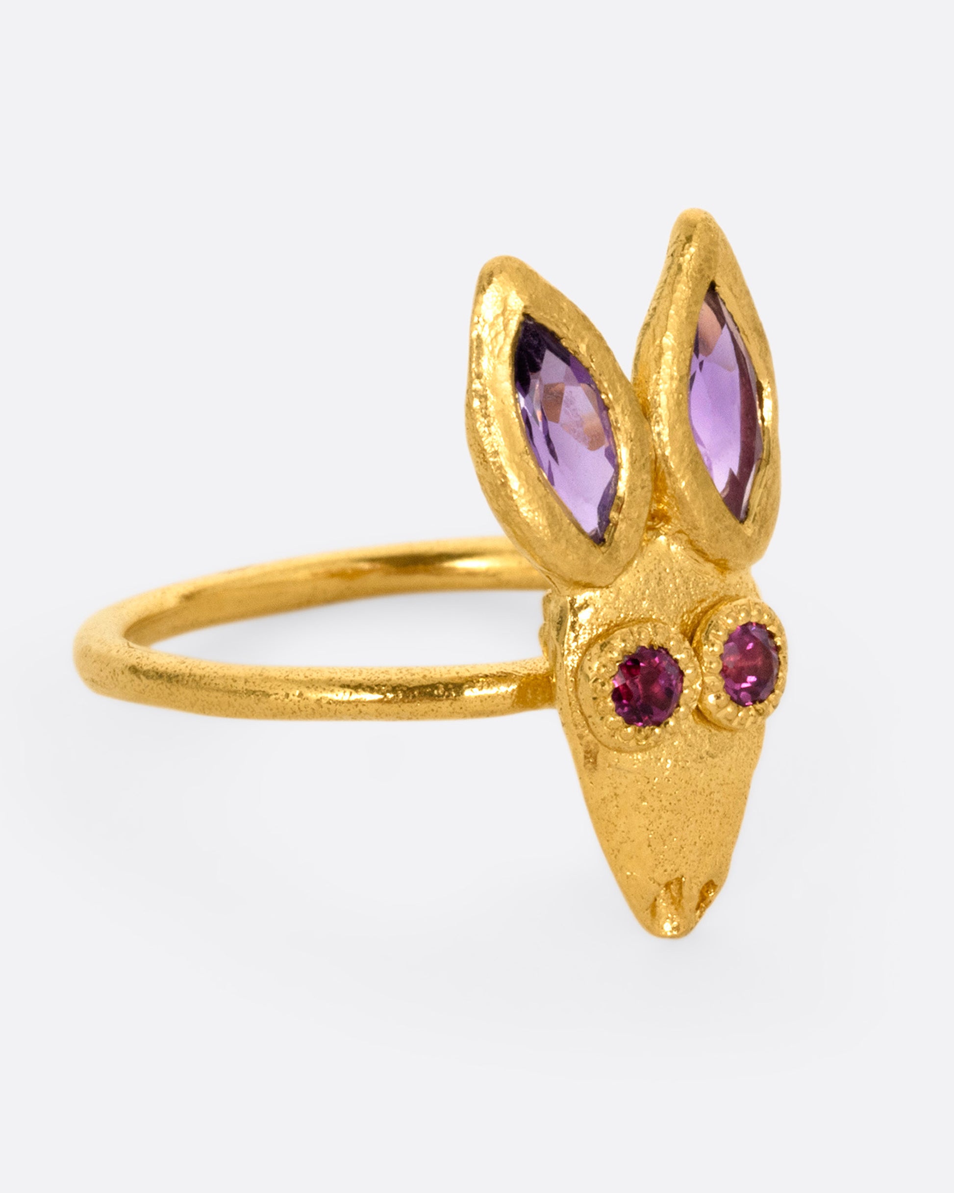 A yellow gold ring with a rabbit face with amethyst ears and tourmaline eyes. Shown from the side.