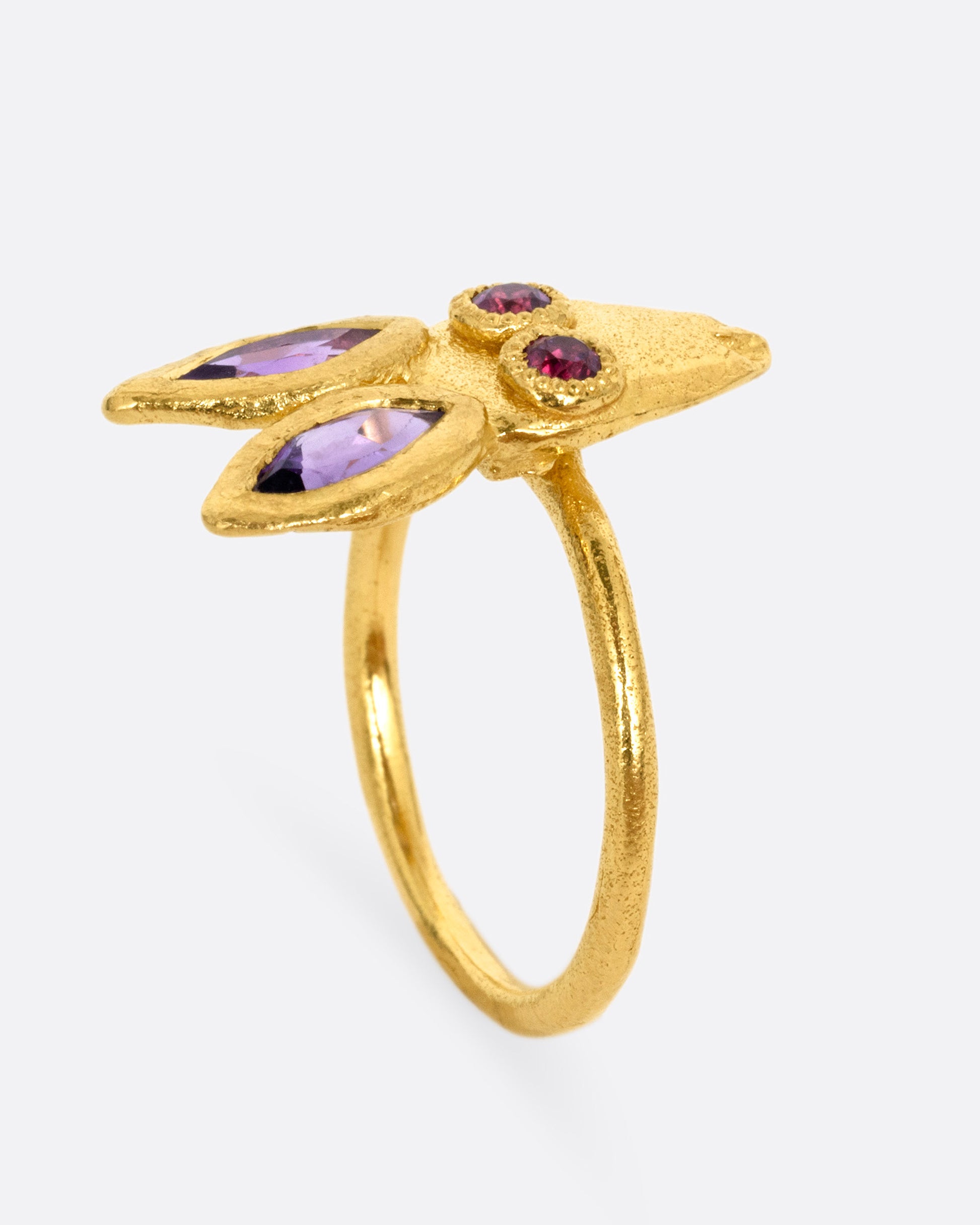 A yellow gold ring with a rabbit face with amethyst ears and tourmaline eyes. Shown from the side standing up.