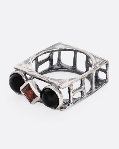A silver square cage ring with two onyx cabochons bookending a princess cut garnet, shown from the side.