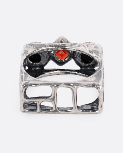 A silver square cage ring with two onyx cabochons bookending a princess cut garnet, shown from the back.
