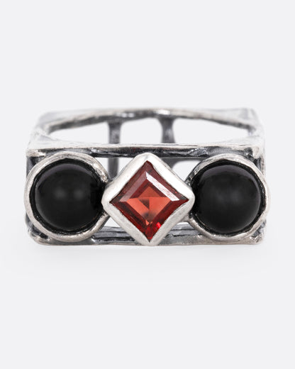 A silver square cage ring with two onyx cabochons bookending a princess cut garnet, shown from the front.