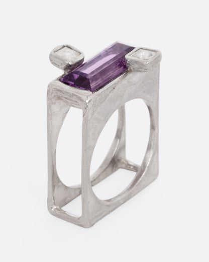 A silver square ring with an amethyst baguette and two square topaz, shown standing up from the side.