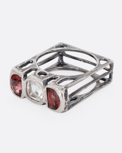 A silver ring with a cushion cut white topaz between two half moon garnets, shown from the side.