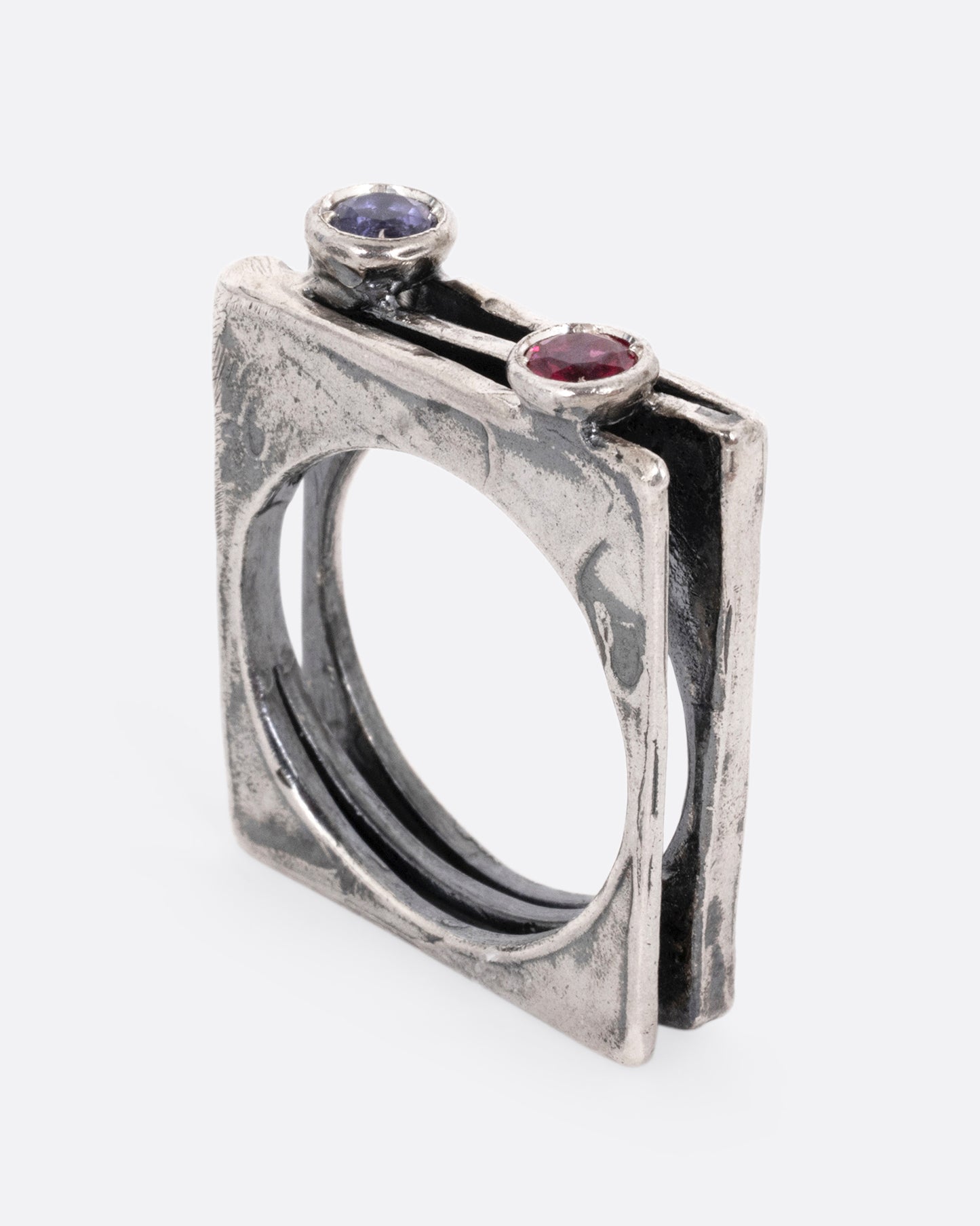 A silver stacked square ring with a blue sapphire and a pink sapphire shown standing up from the side.