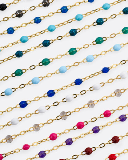 A photo of numerous yellow gold chains with different colors of resin beads.