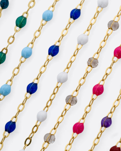 A close up of numerous yellow gold chains with different colors of resin beads.