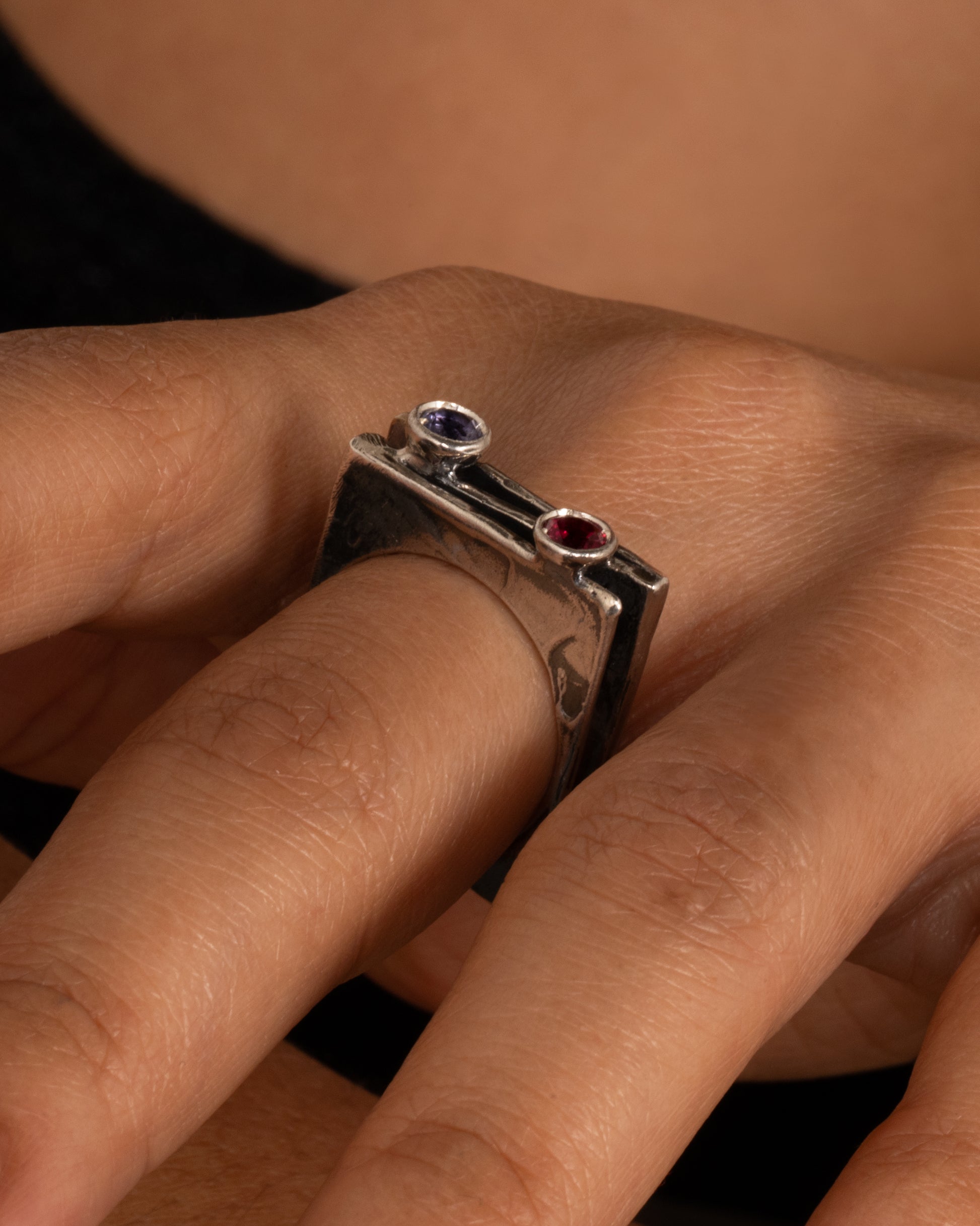 A silver stacked square ring with a blue sapphire and a pink sapphire shown on a hand.
