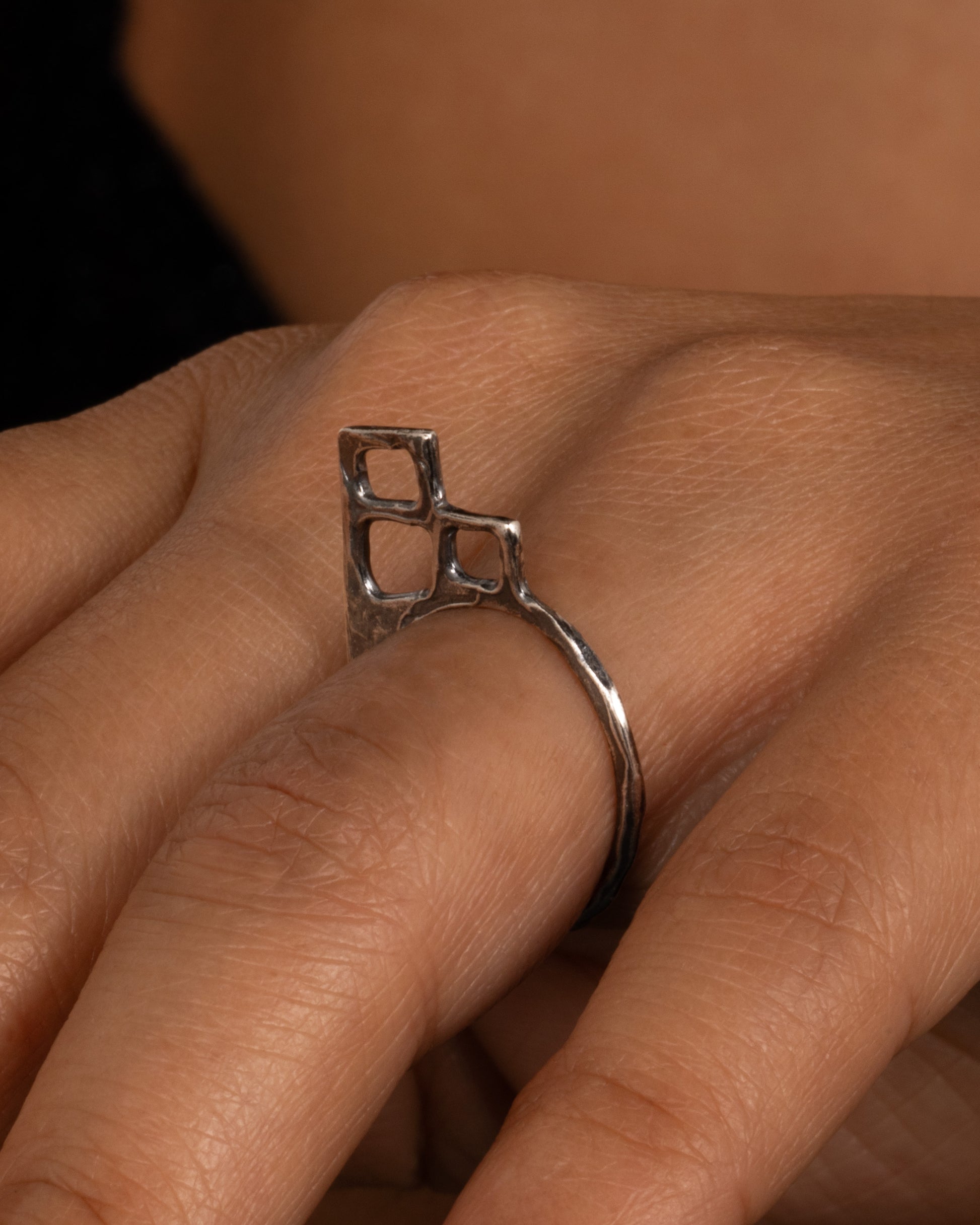 A silver ring with trio of stacked open windows, shown on a hand.